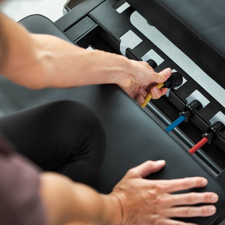 Person adjusting resistance bands on an exercise bench.