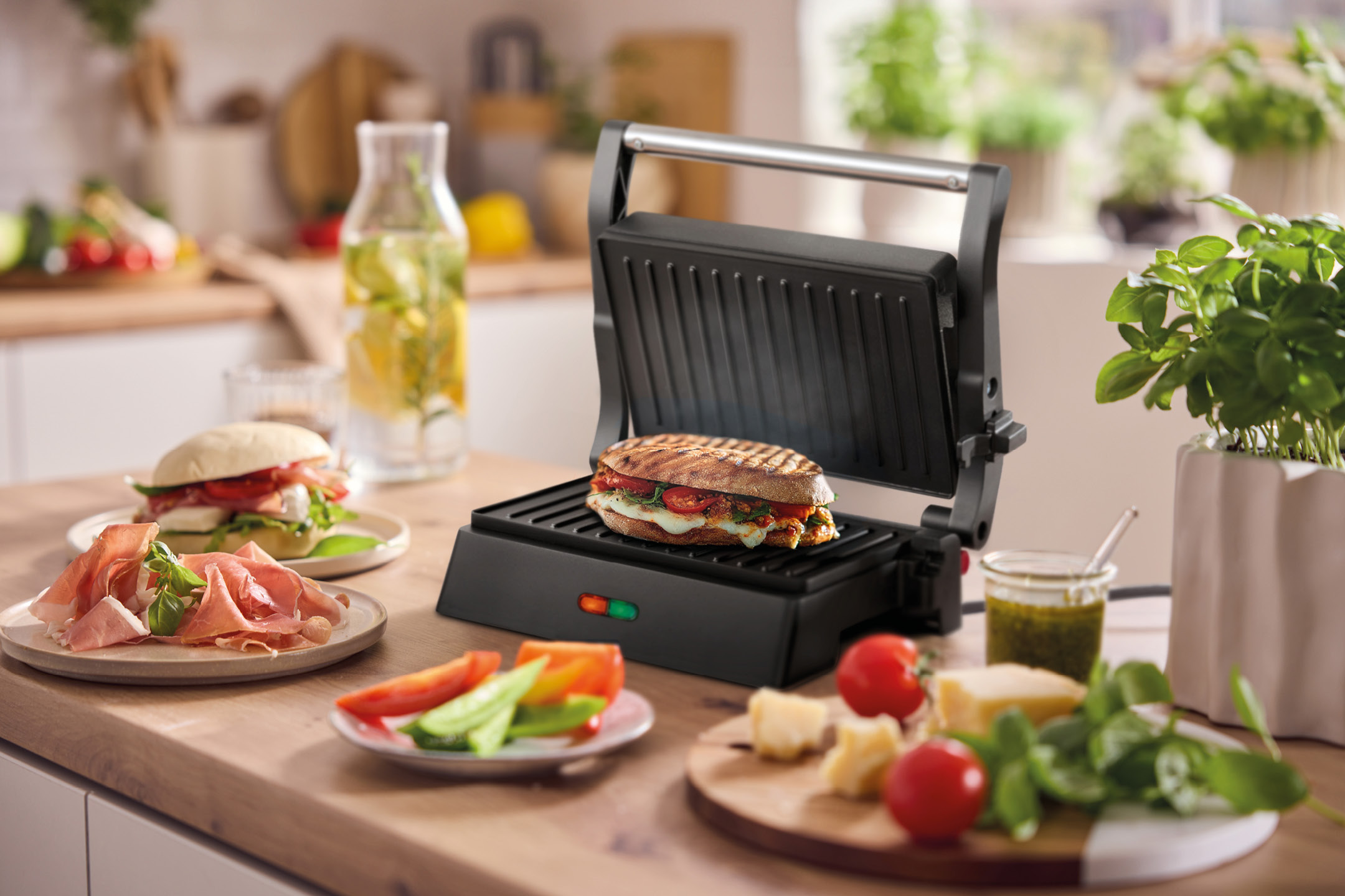 Panini press with a grilled sandwich, surrounded by fresh ingredients on a kitchen counter.