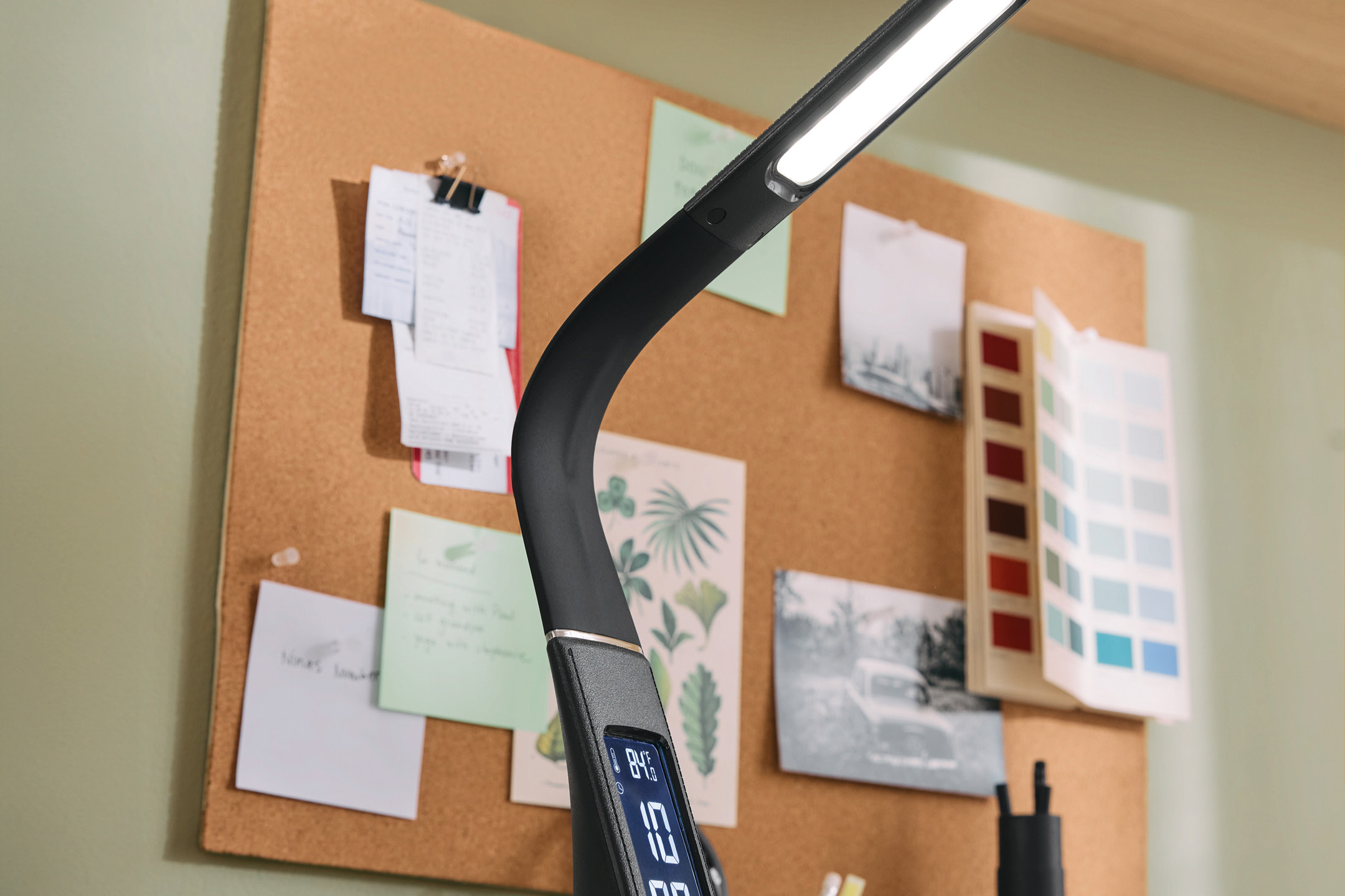 Desk lamp with digital display on a cork board background with notes and color swatches.