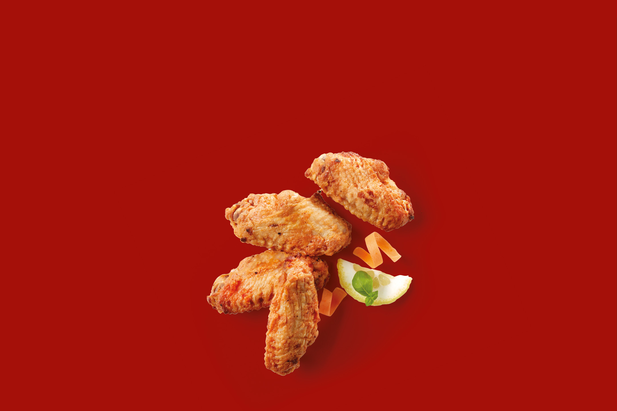 Crispy fried chicken wings with lemon and carrot garnish on a red background.