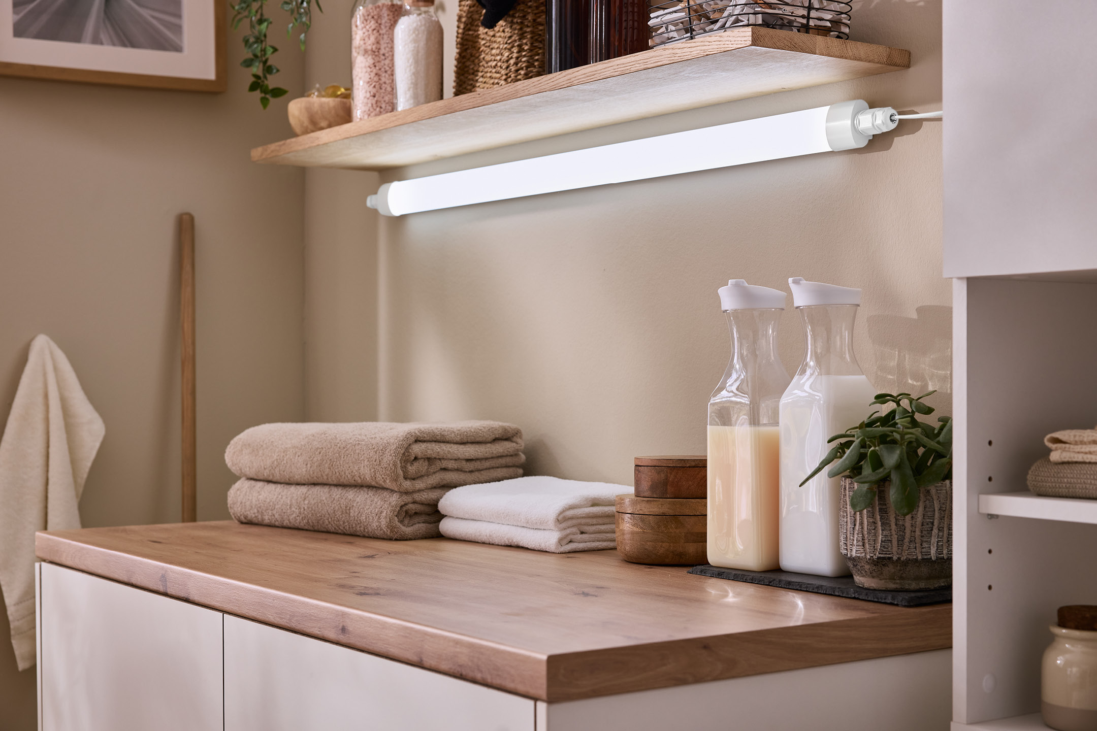 Laundry room with wooden countertop, towels, and laundry detergents under a shelf light.