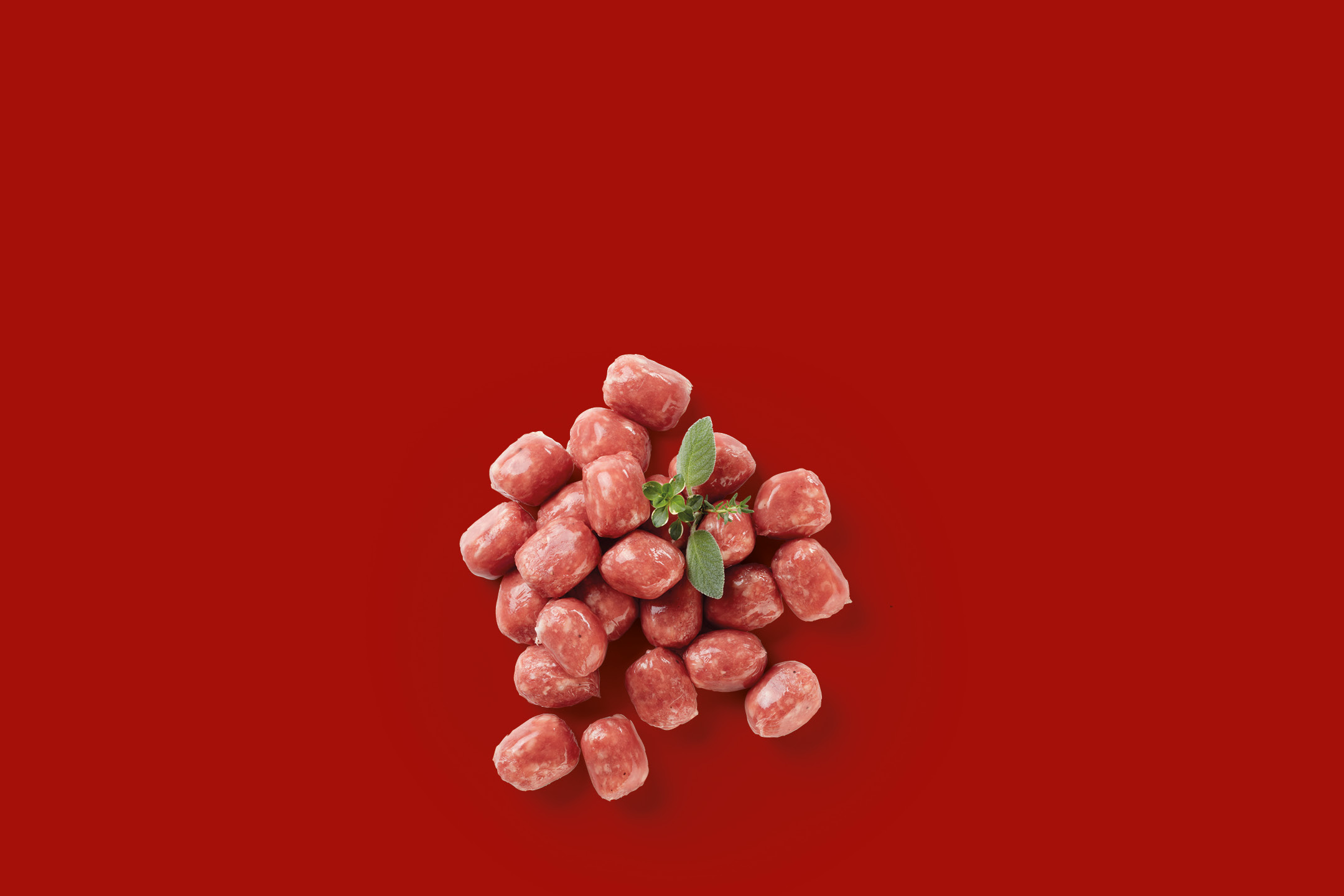 Small raw sausages with herbs on a red background.