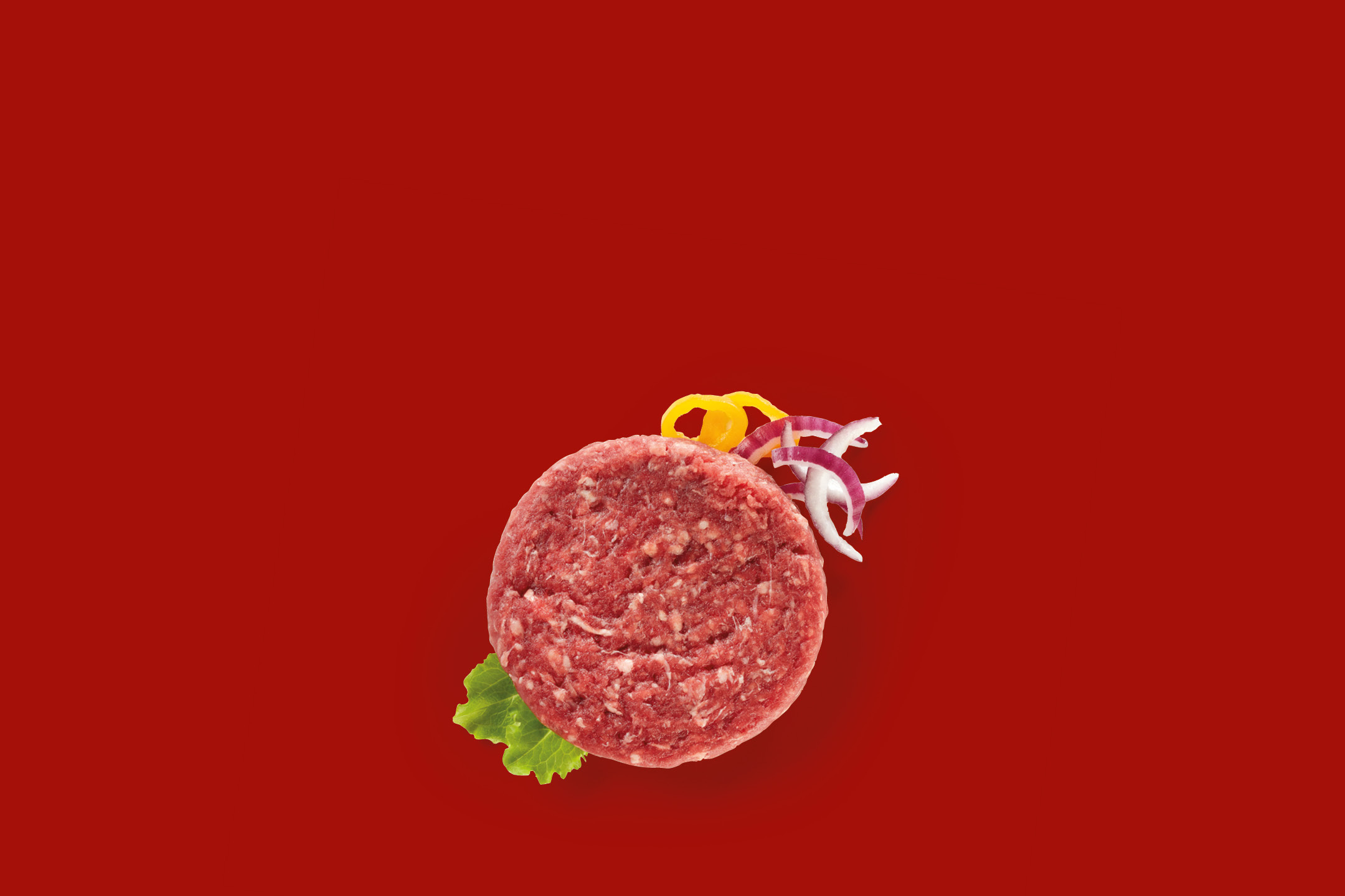 Raw beef burger patty with lettuce, red onion, and yellow pepper on a red background.