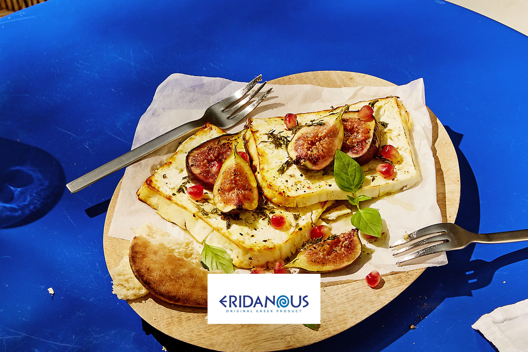 Eridanous grilled halloumi with figs, pomegranate, and herbs on a blue table.