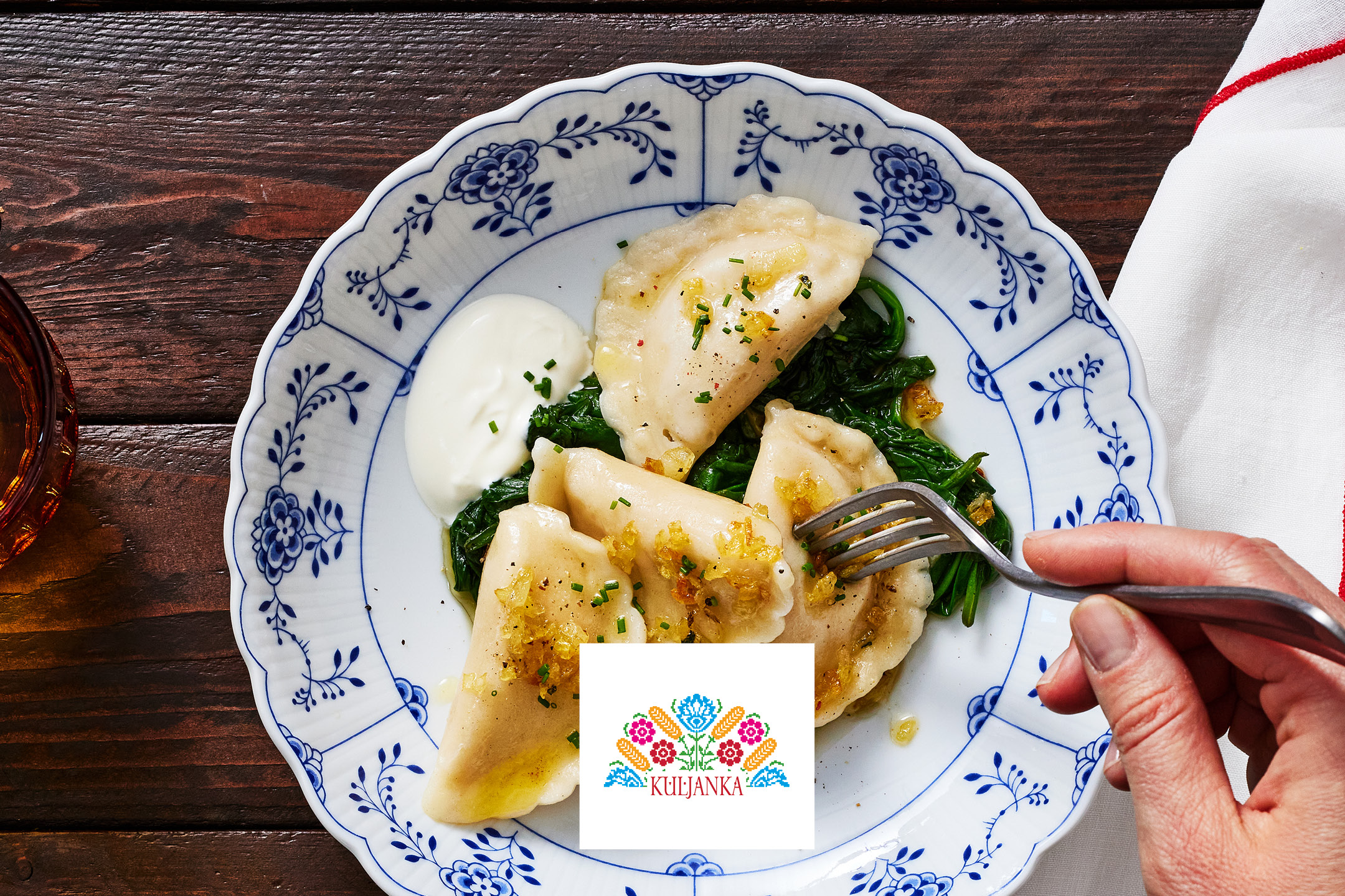 Pierogi with spinach, sour cream, and fried onions on a white and blue plate.