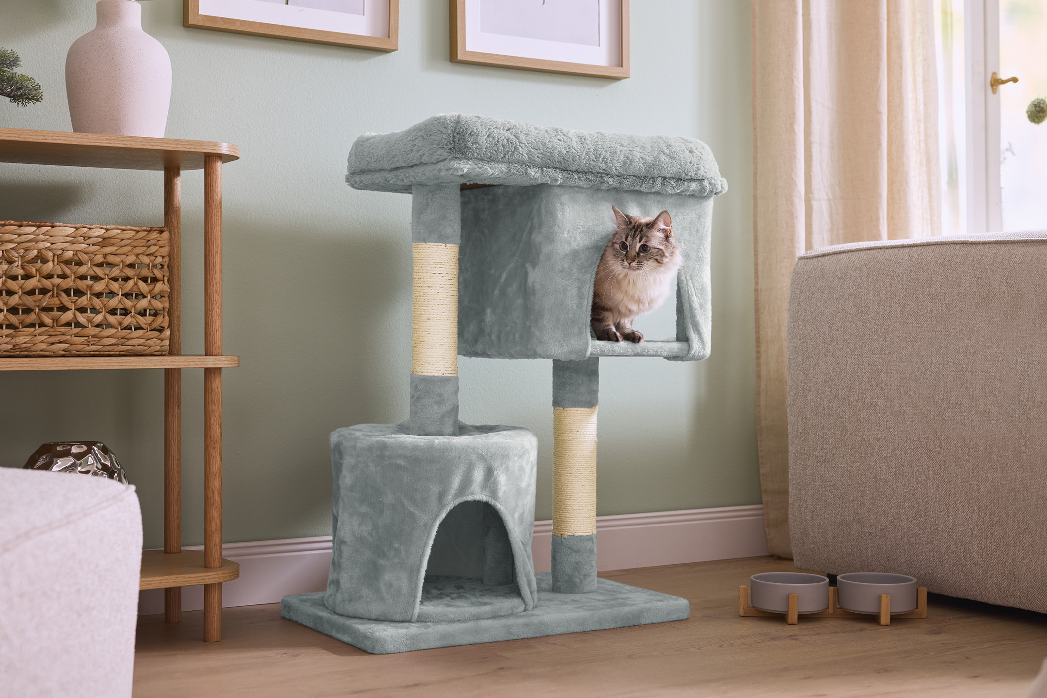 A cat tree with a cat inside, next to a wooden shelf and a sofa.