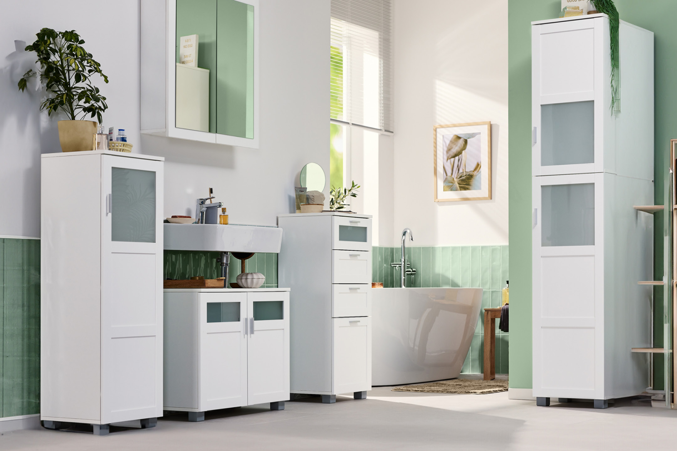 White bathroom furniture set with tall cabinets, vanity unit, and bathtub in a modern bathroom.