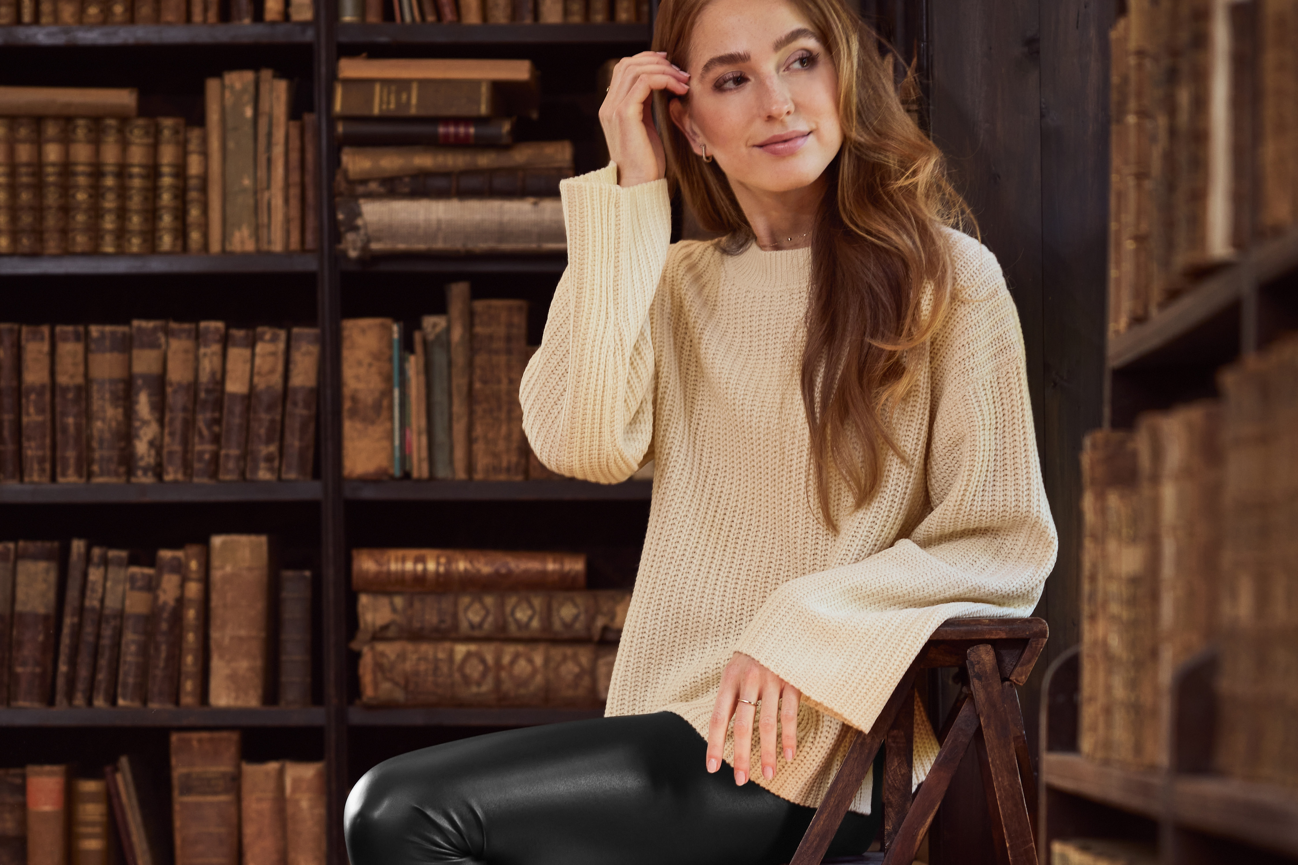 Woman in a cream sweater and black leggings sitting in a library.