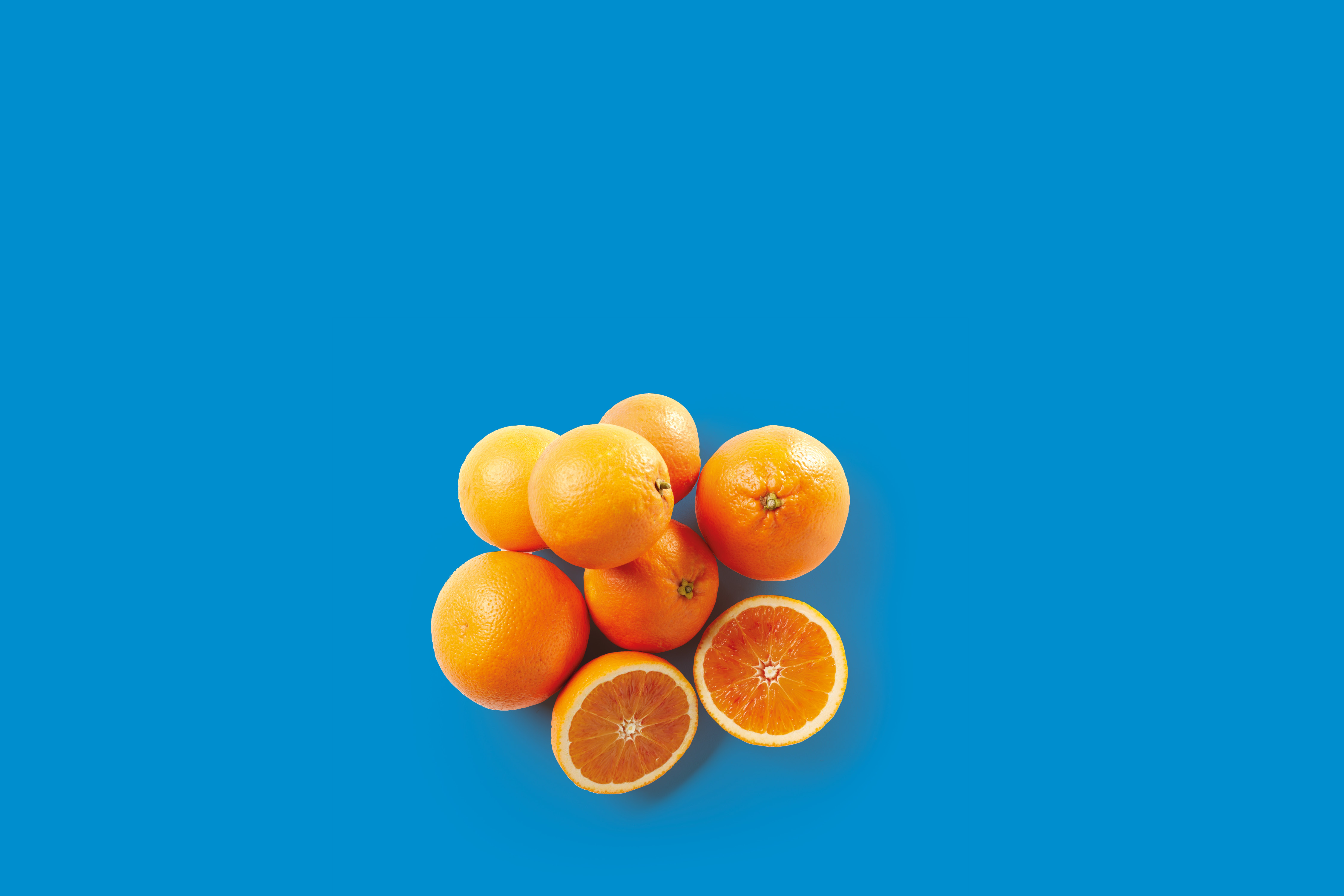 A cluster of whole and halved oranges on a vibrant blue background.