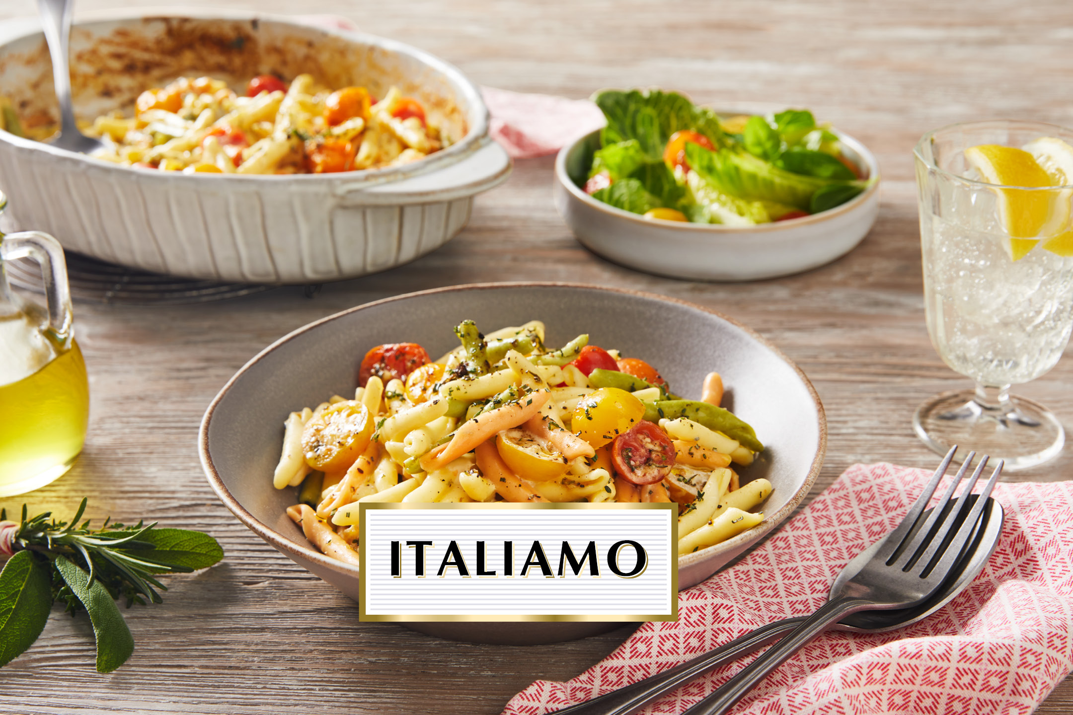 Pasta dish with tomatoes and herbs, salad, and sparkling water, with 'ITALIAMO' text.