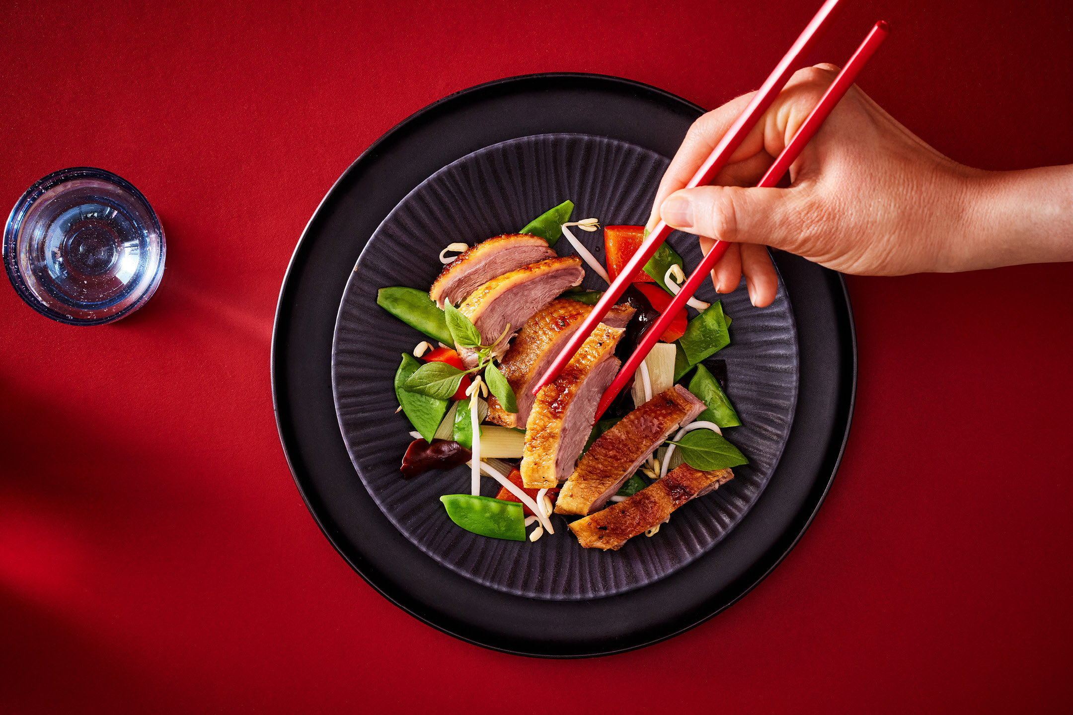 Crispy duck breast with stir-fried vegetables and red chopsticks on a black plate.