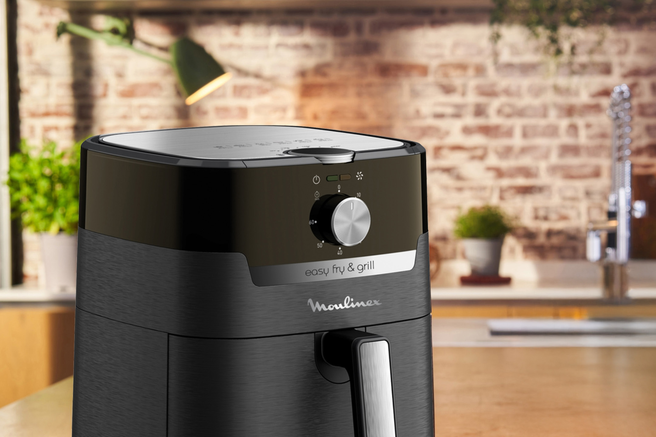 Black air fryer with a silver handle and control knob on a wooden counter in a kitchen.