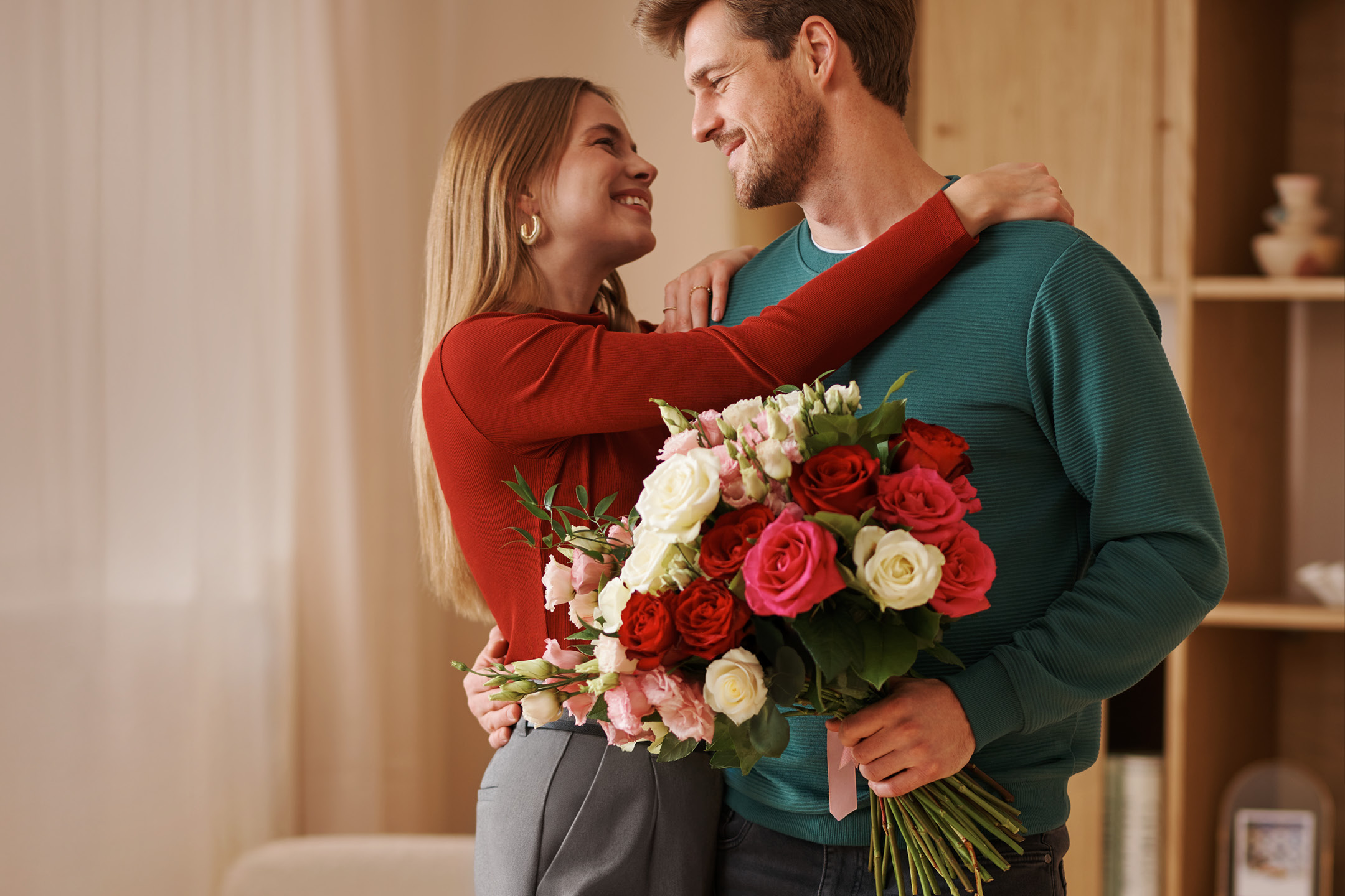 A couple embracing, holding a vibrant bouquet of red, pink, and white roses.