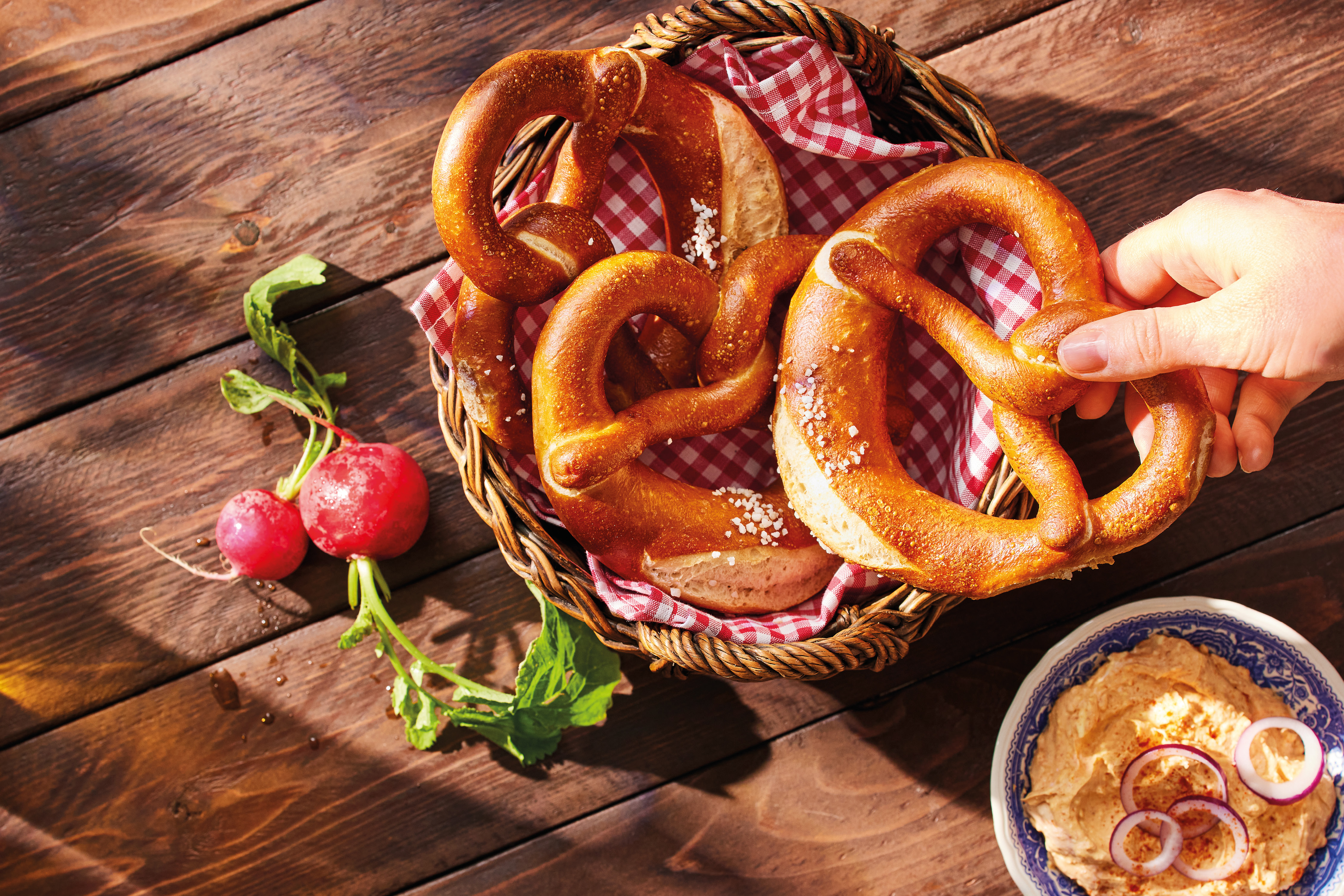 Pretzels in a basket with radishes and a dip on a wooden table.