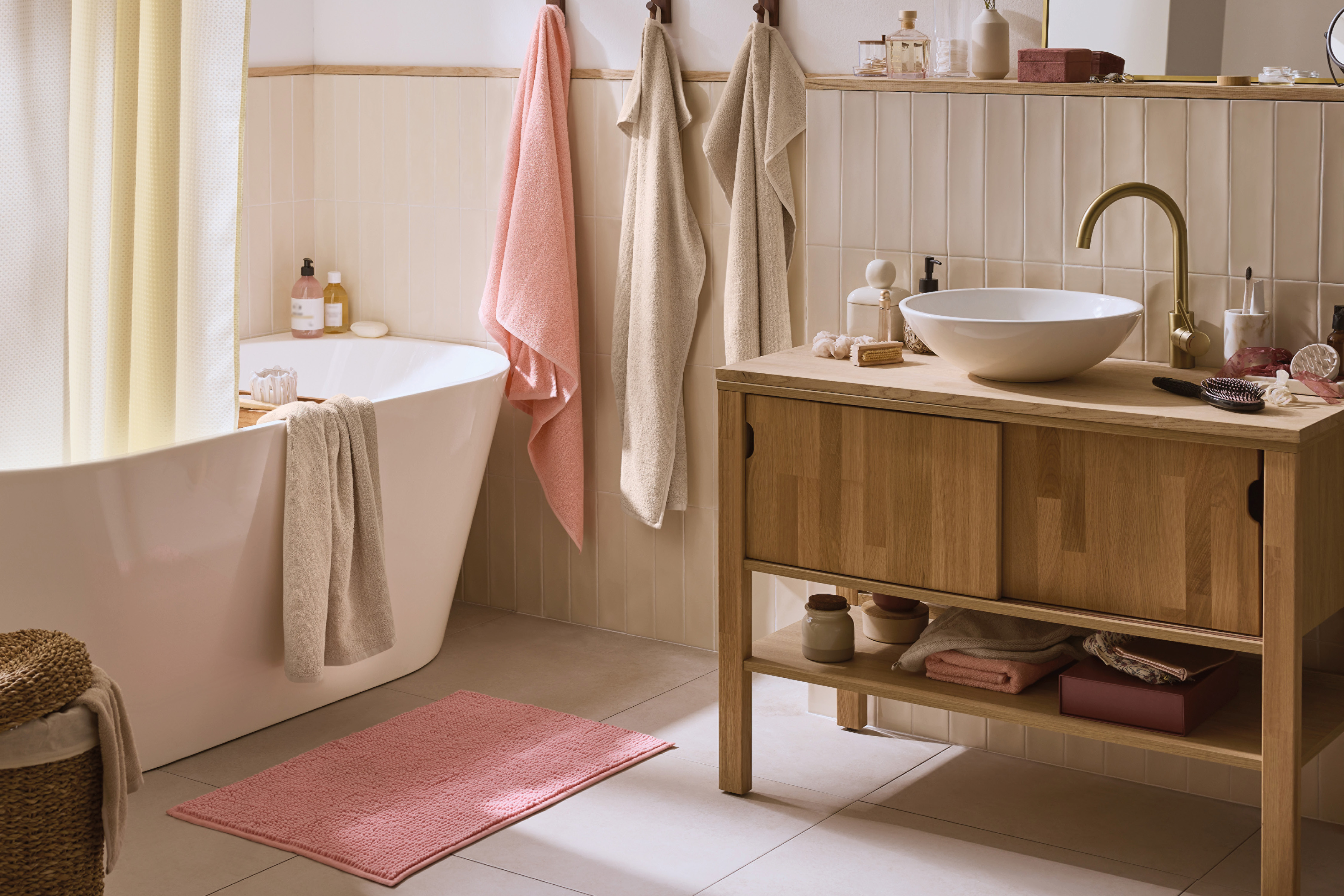 Bathroom with a white bathtub, wooden vanity with a sink, and pink bath mat.