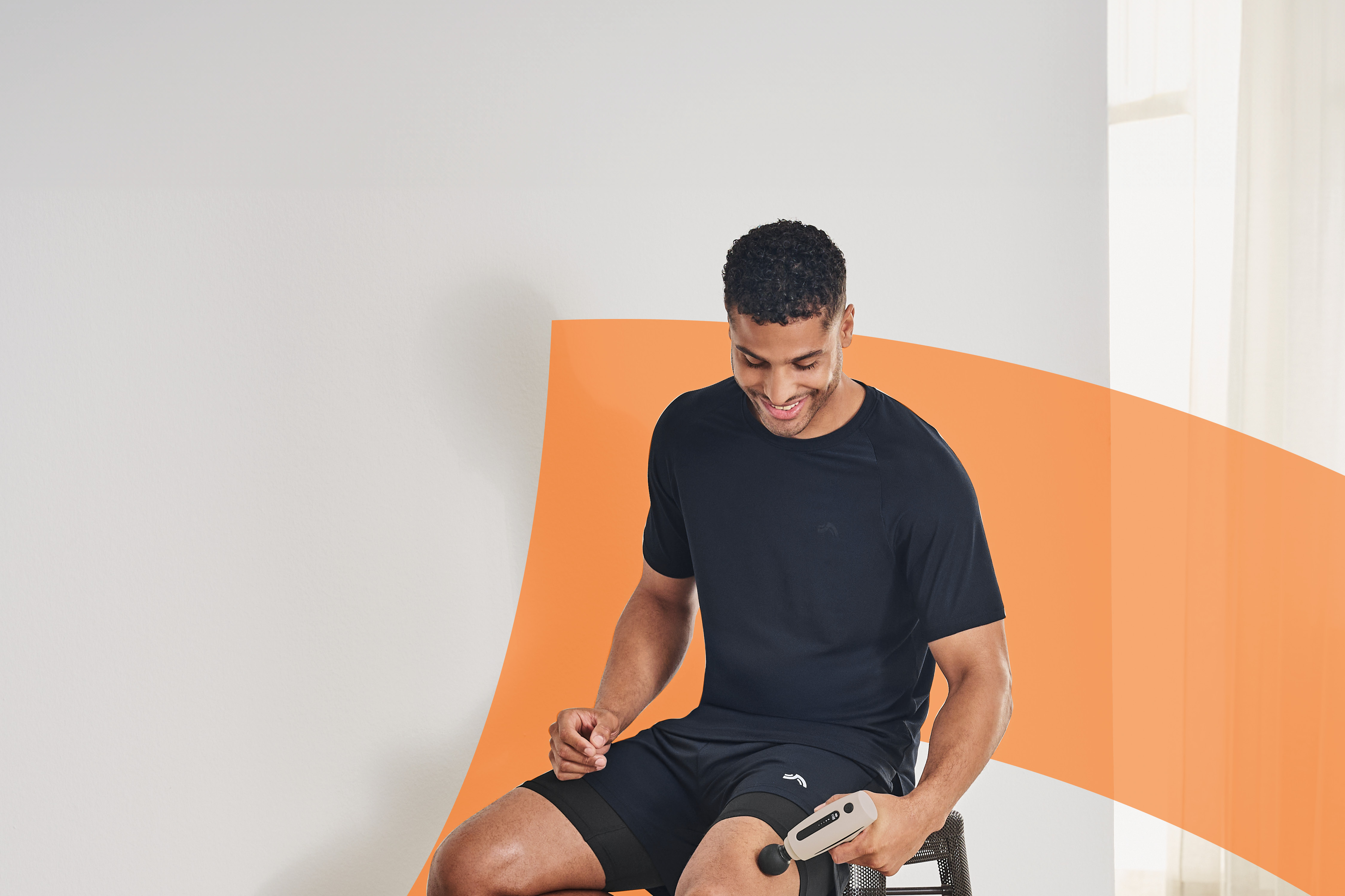 Man in athletic wear using a massage gun on his thigh.