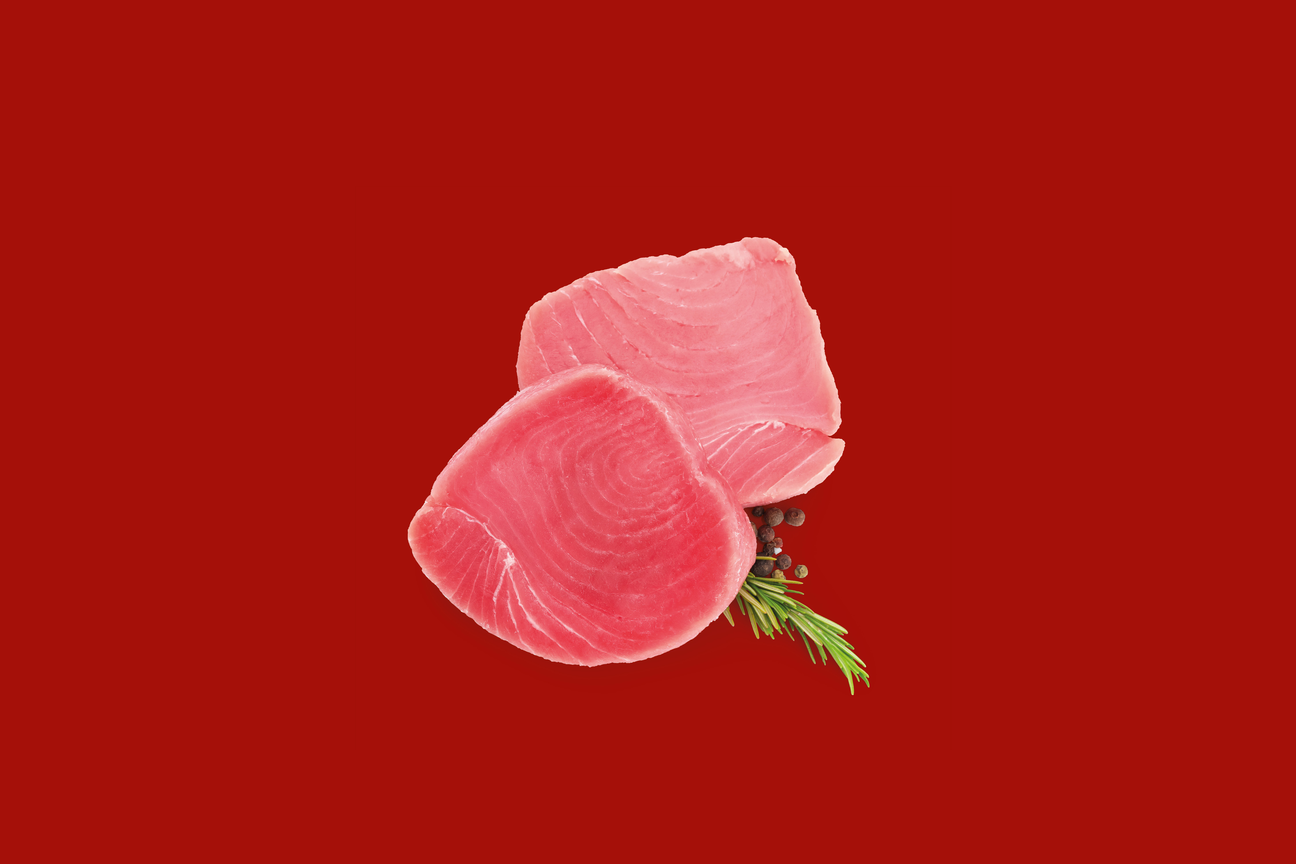 Two fresh tuna steaks with rosemary and peppercorns on a red background.