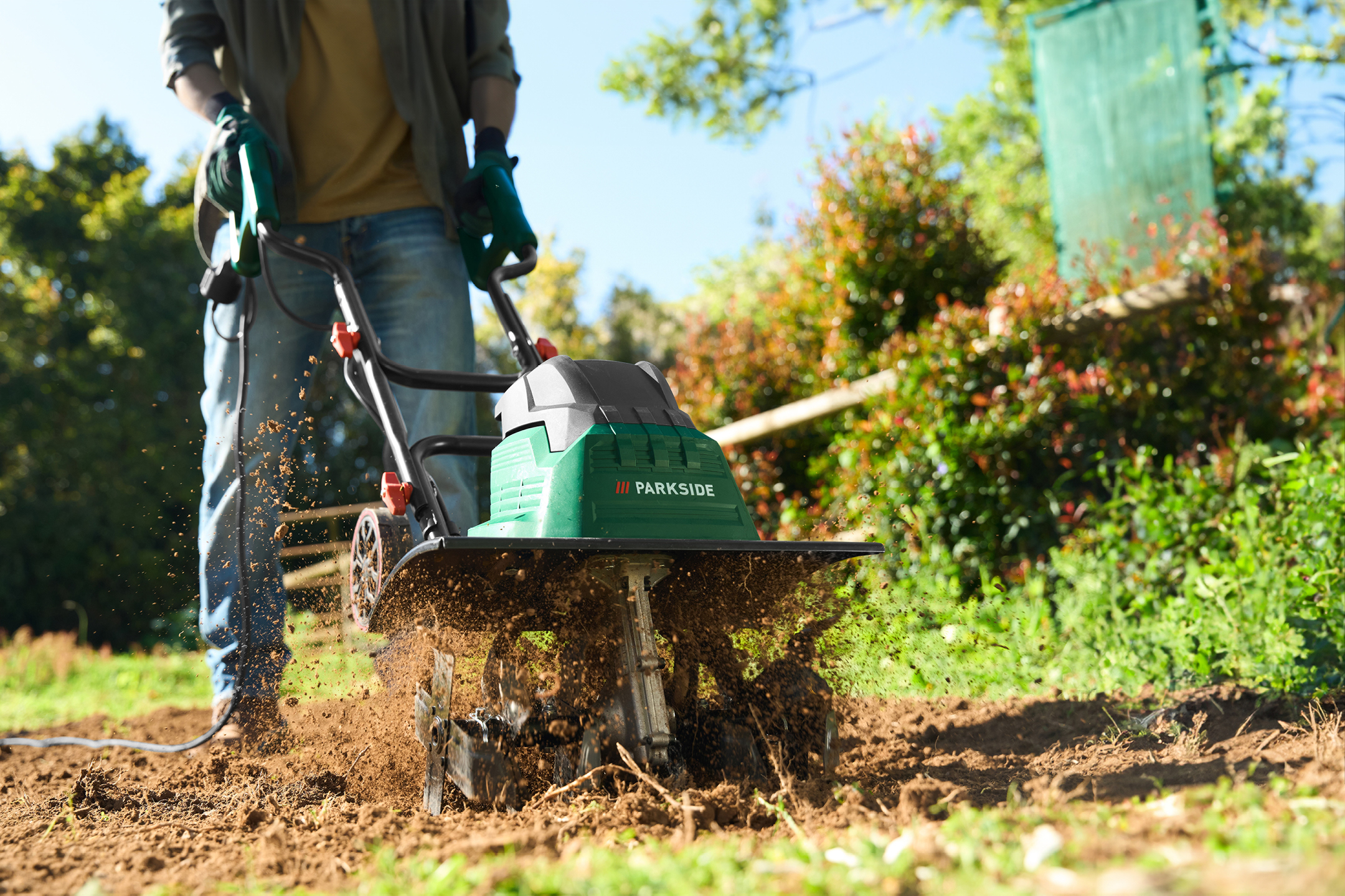 Person using a green electric tiller to cultivate soil in a garden.