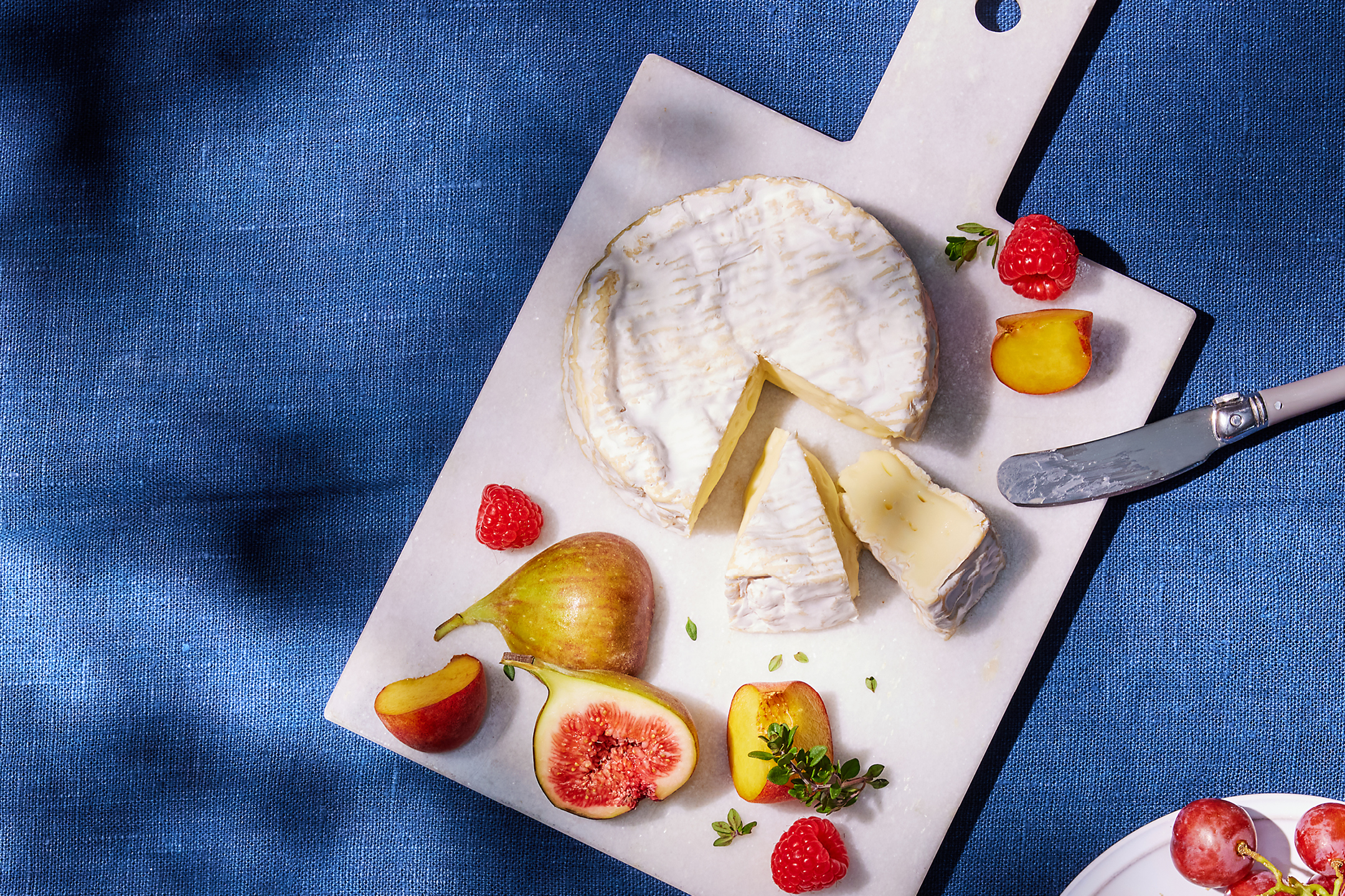 Brie cheese with figs, raspberries, and peaches on a marble board.