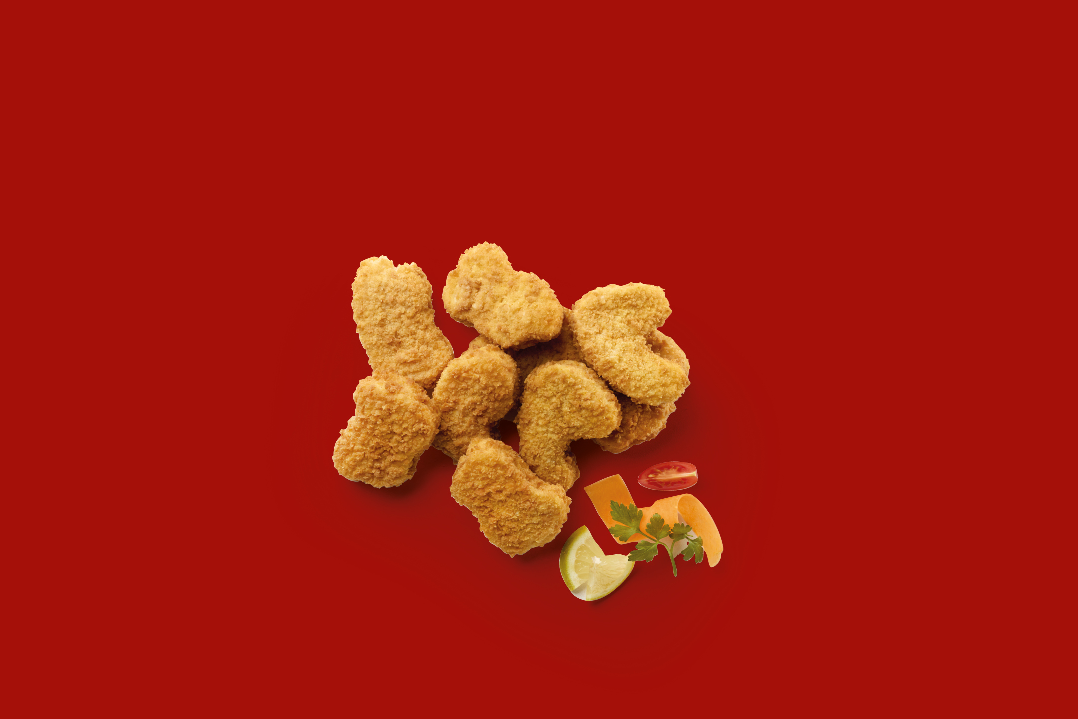 Crispy chicken nuggets with lemon, parsley, carrot, and tomato on a red background.