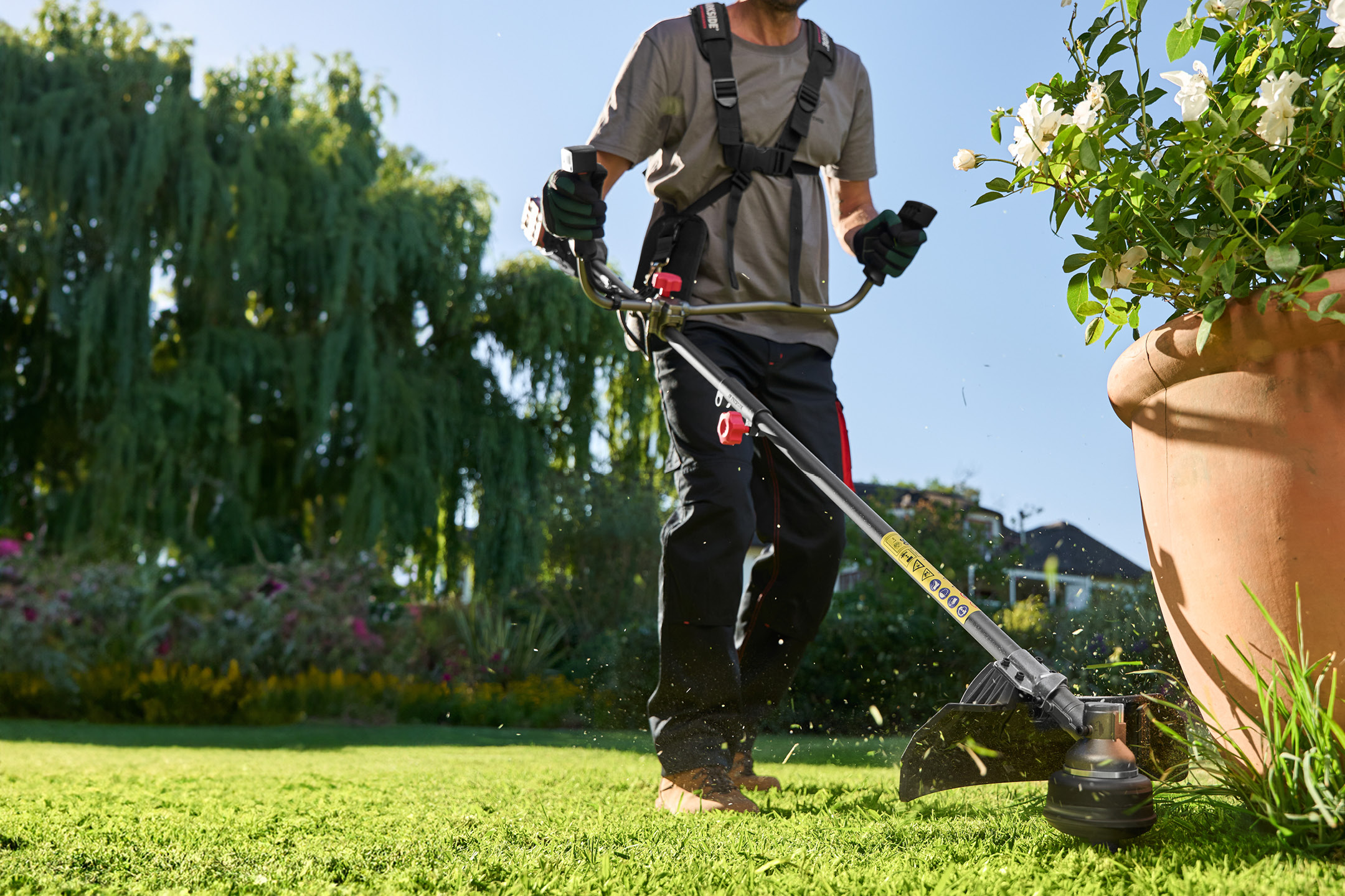Man using a grass trimmer in a garden, cutting grass around a large plant pot.