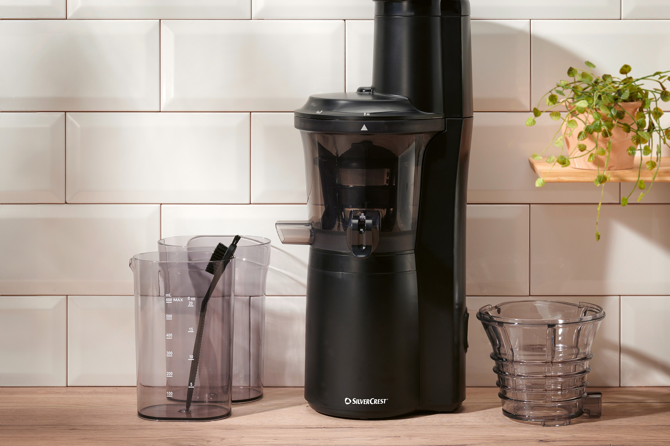 Black slow juicer with measuring cups and a cleaning brush on a wooden counter.