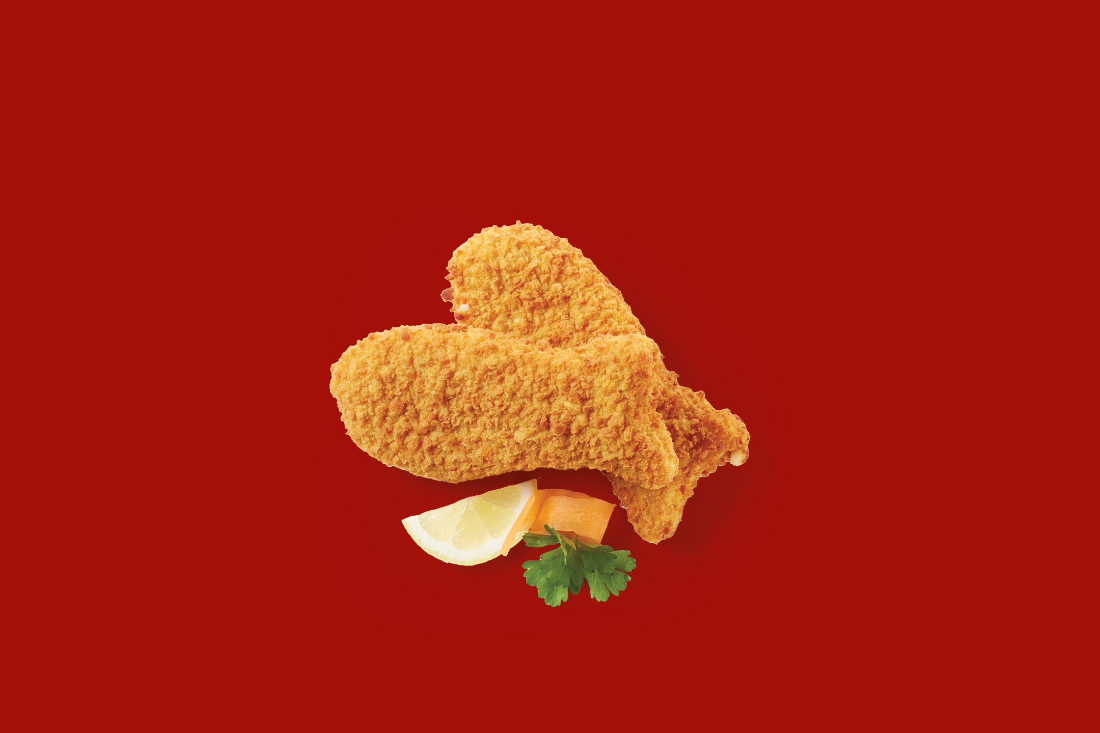 Two breaded fish fillets with a lemon wedge, carrot slice, and parsley on a red background.