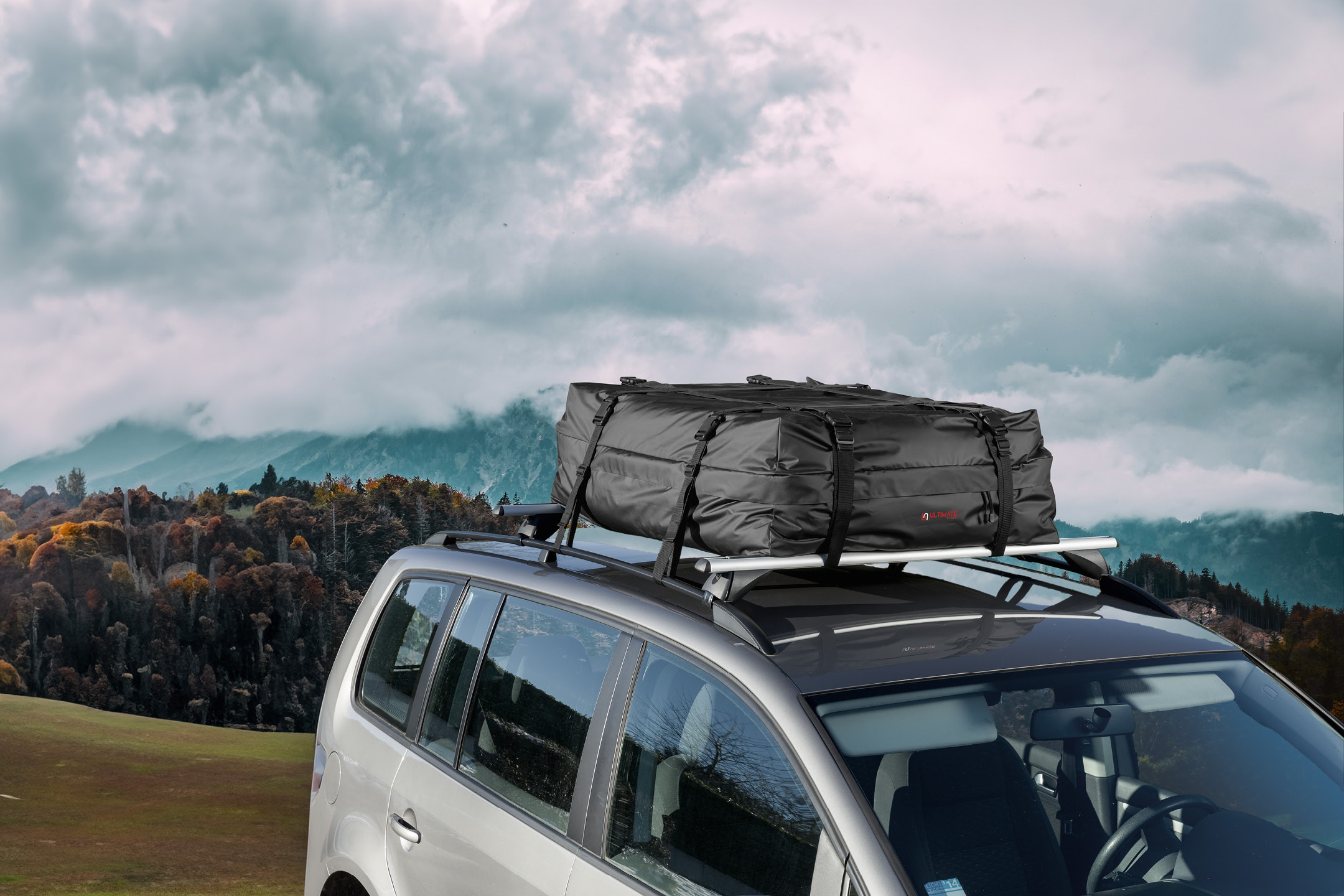 Car with a black roof bag on a roof rack, parked in a mountainous landscape.