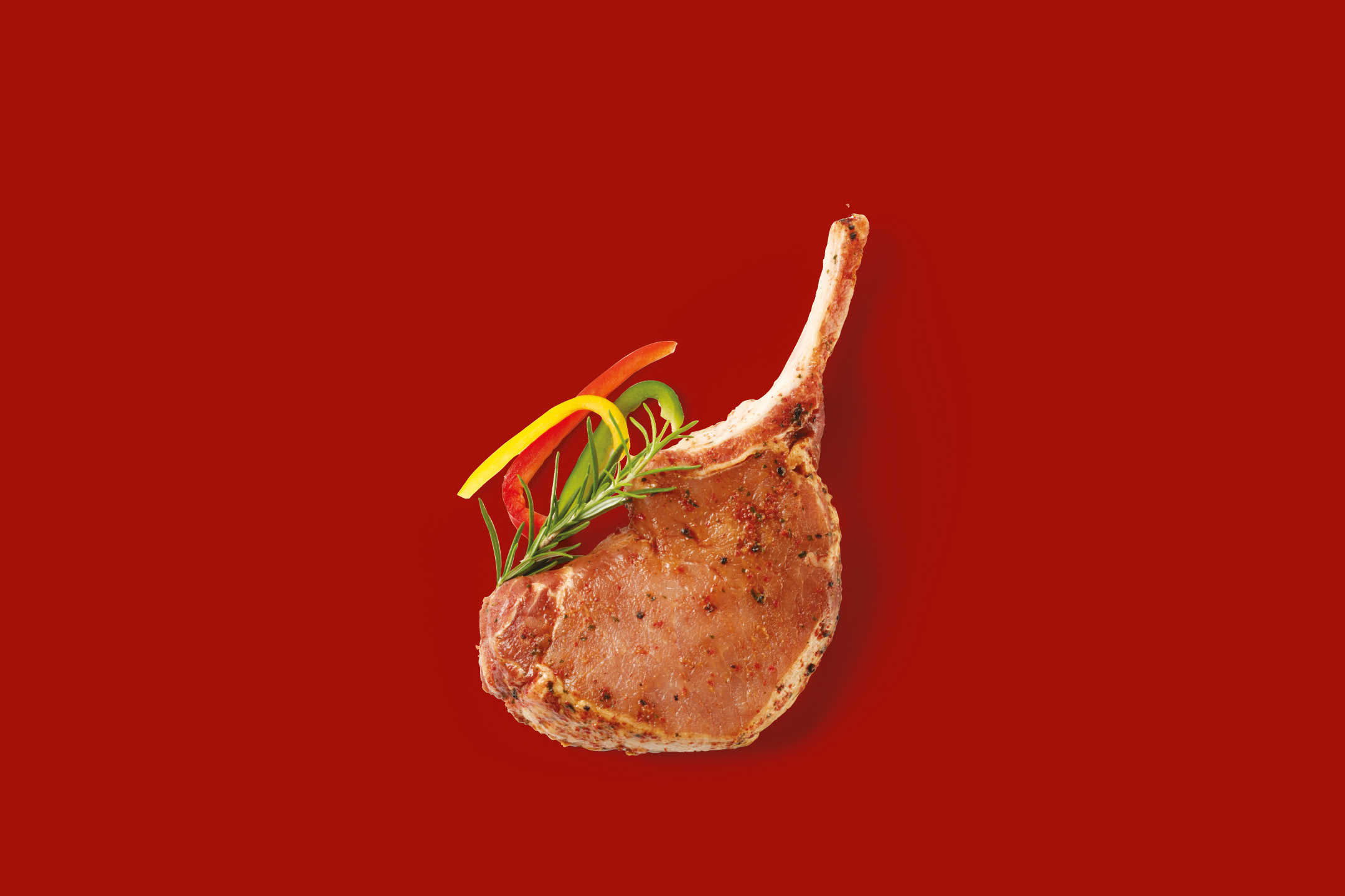 Raw pork chop with rosemary and bell pepper strips on a red background.