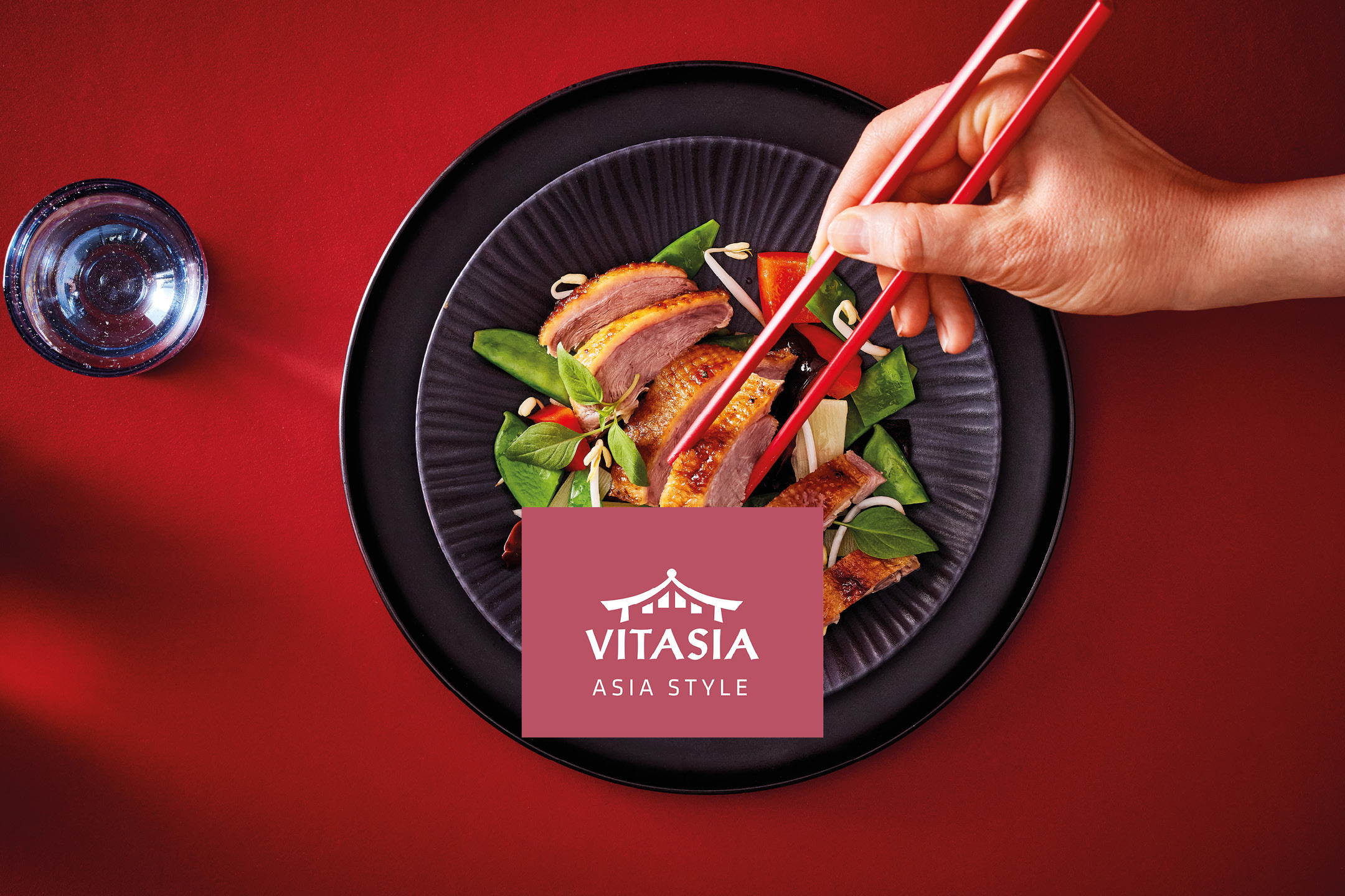 Duck breast with vegetables on a black plate, with a hand holding red chopsticks.