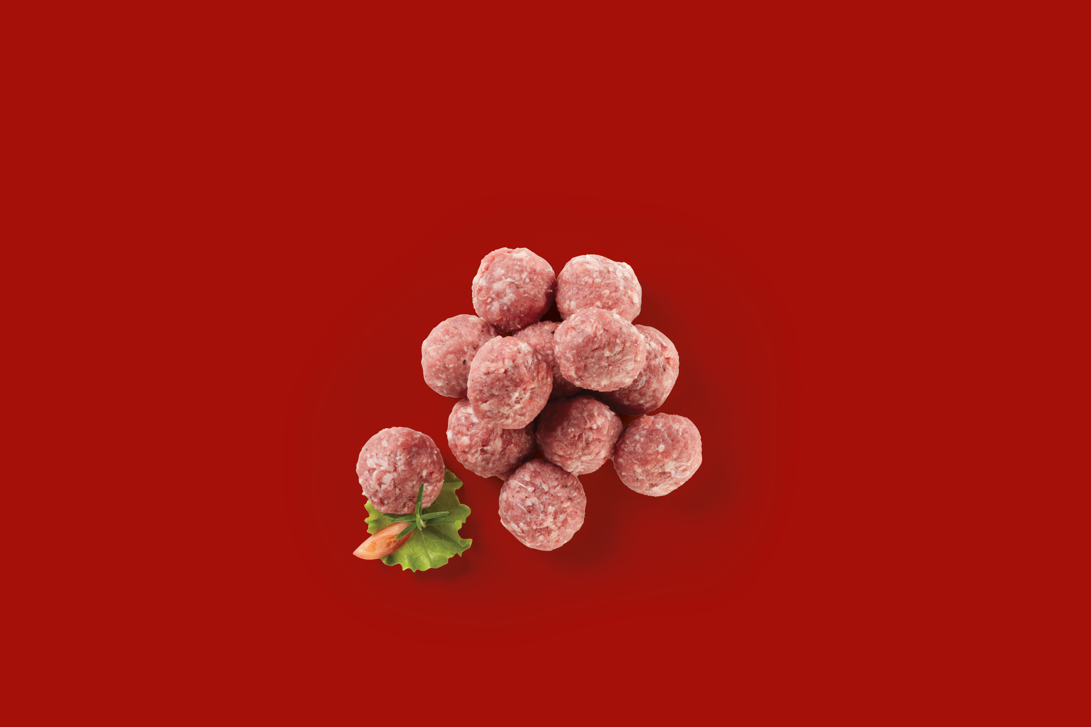 Pile of raw meatballs with a garnish of lettuce and tomato on a red background.