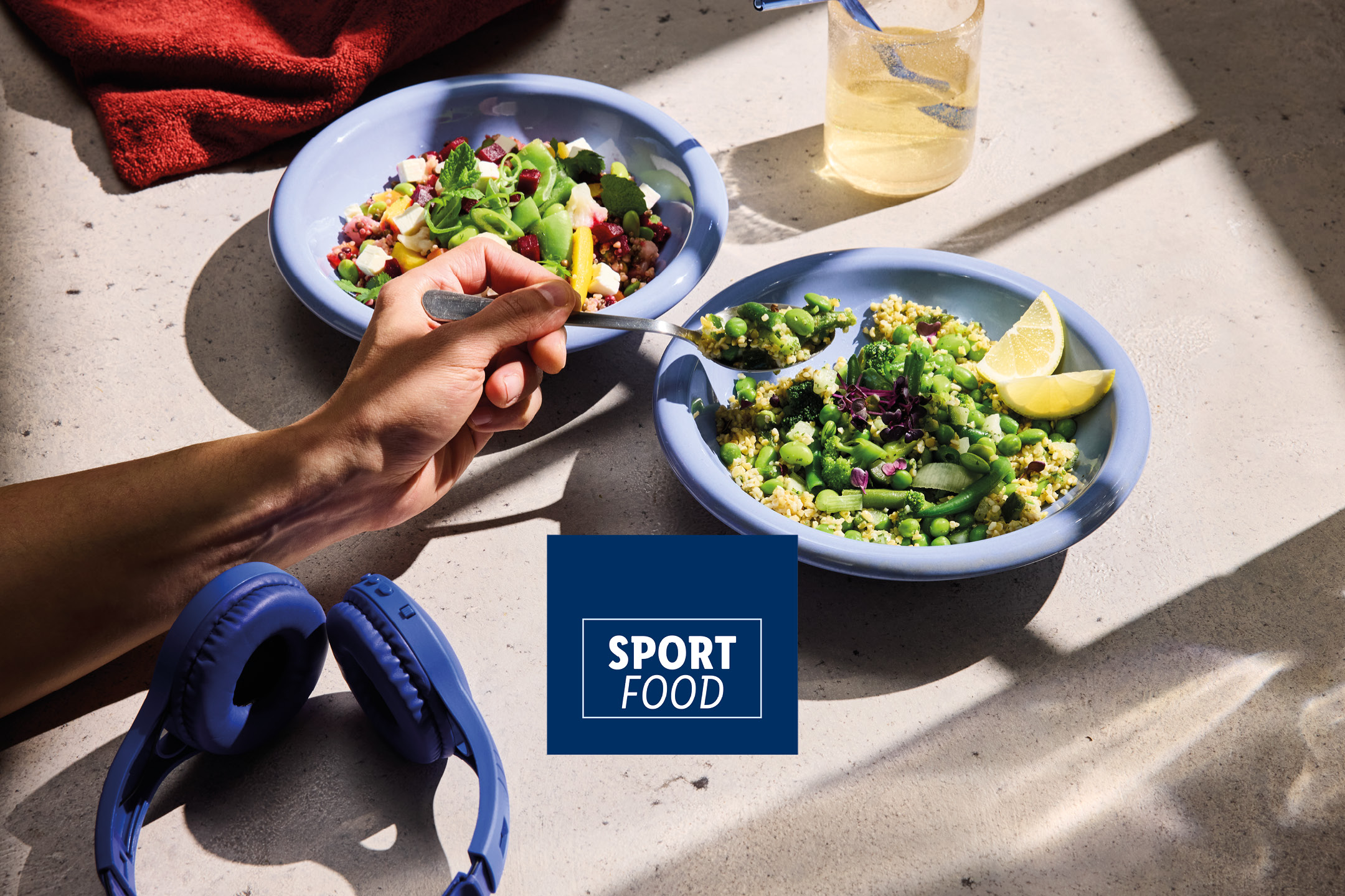 Two bowls of healthy salads, a glass of water, and headphones on a sunlit table. Text: SPORT FOOD.
