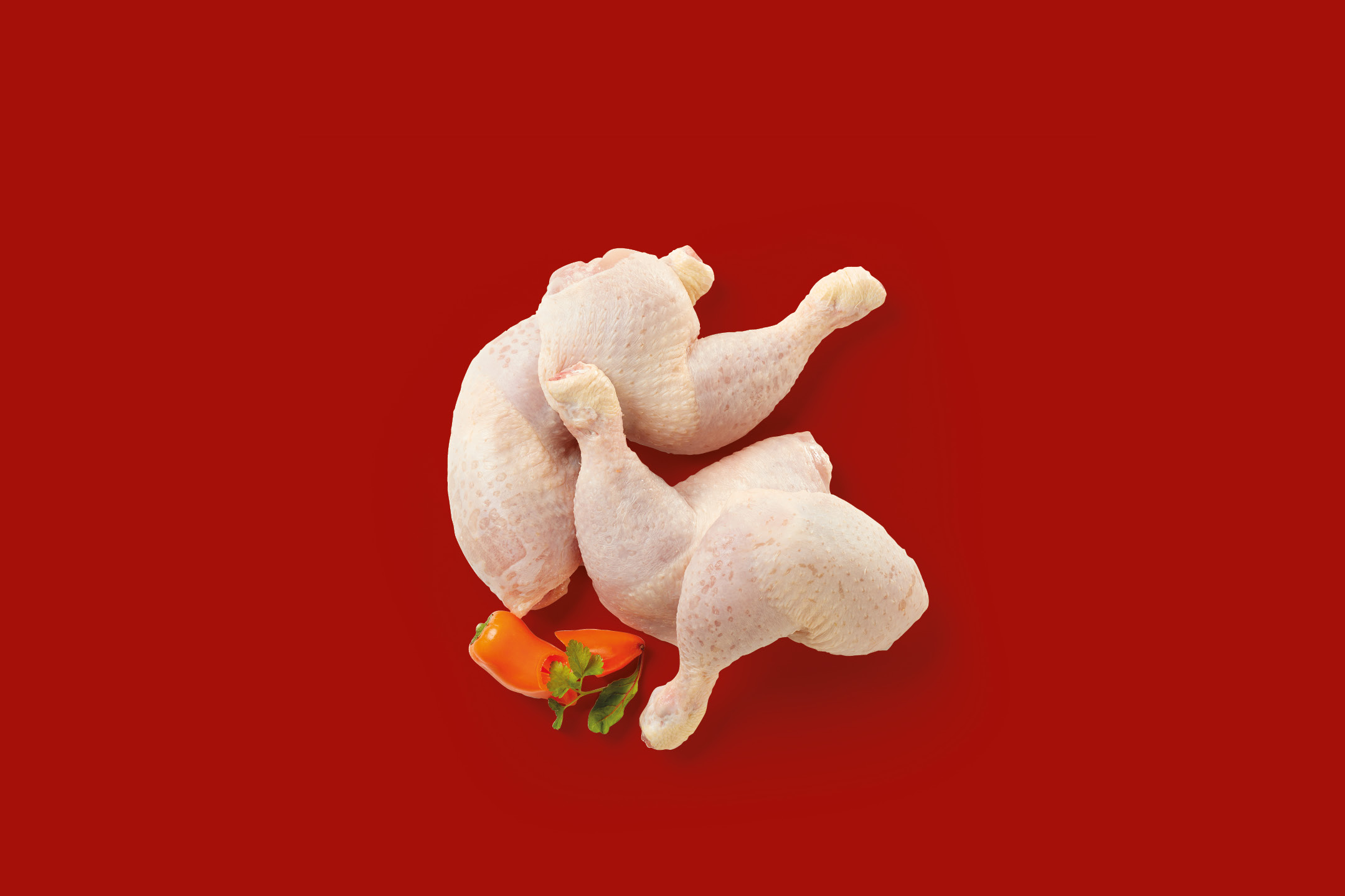 Raw chicken leg quarters with orange peppers and parsley on a red background.