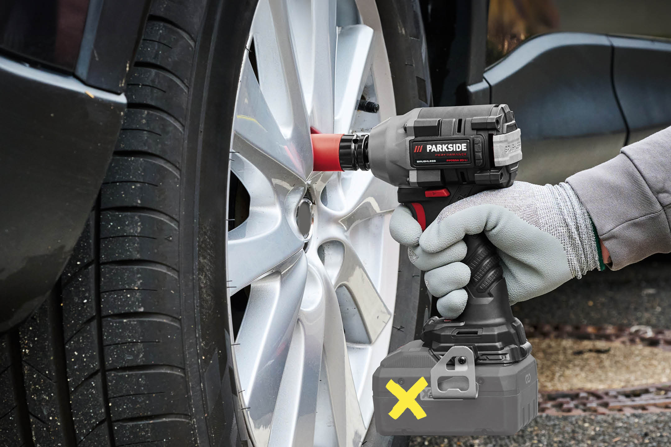 Cordless impact wrench with a red socket removing a car wheel.
