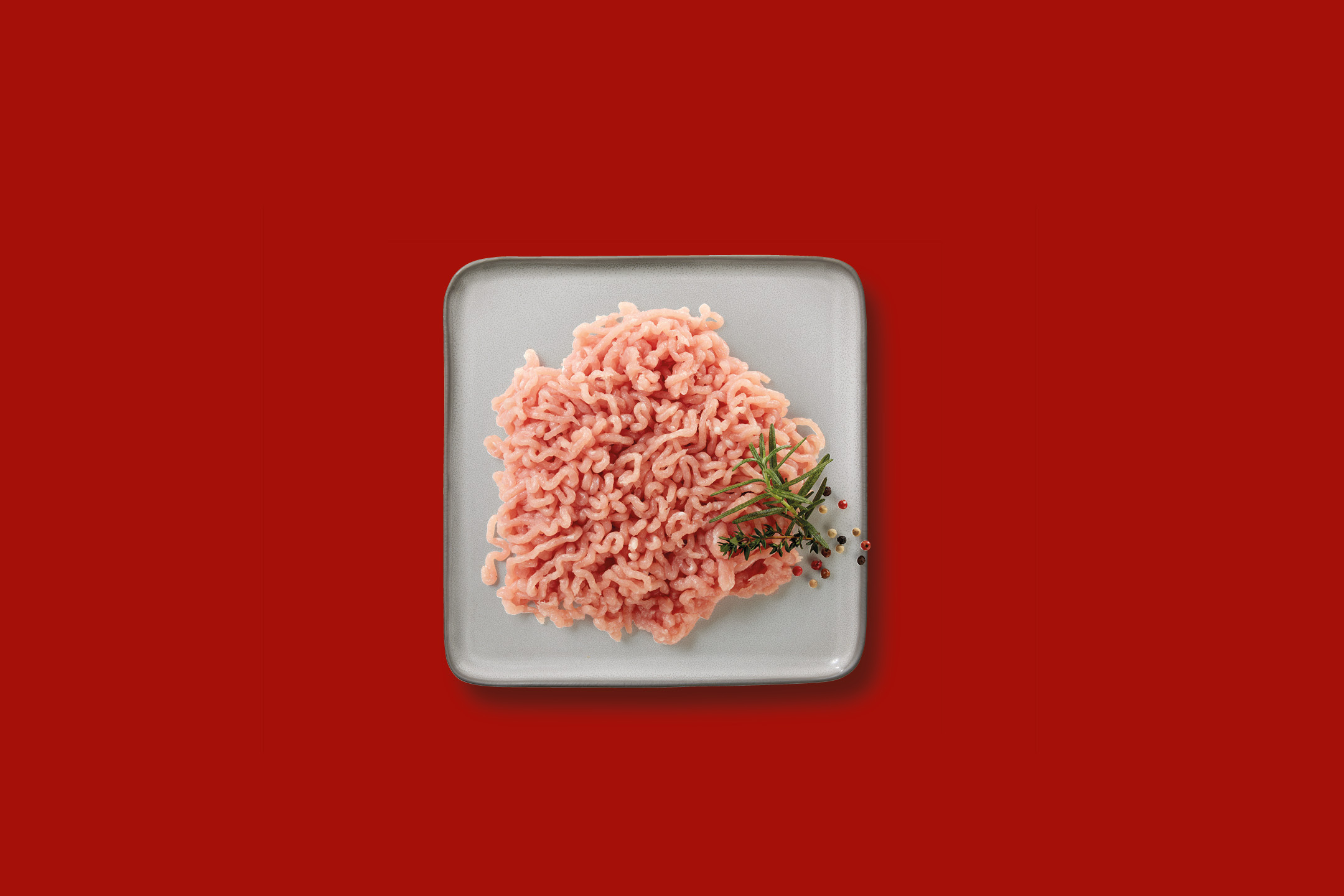 Minced chicken or turkey meat with rosemary and peppercorns on a gray plate.