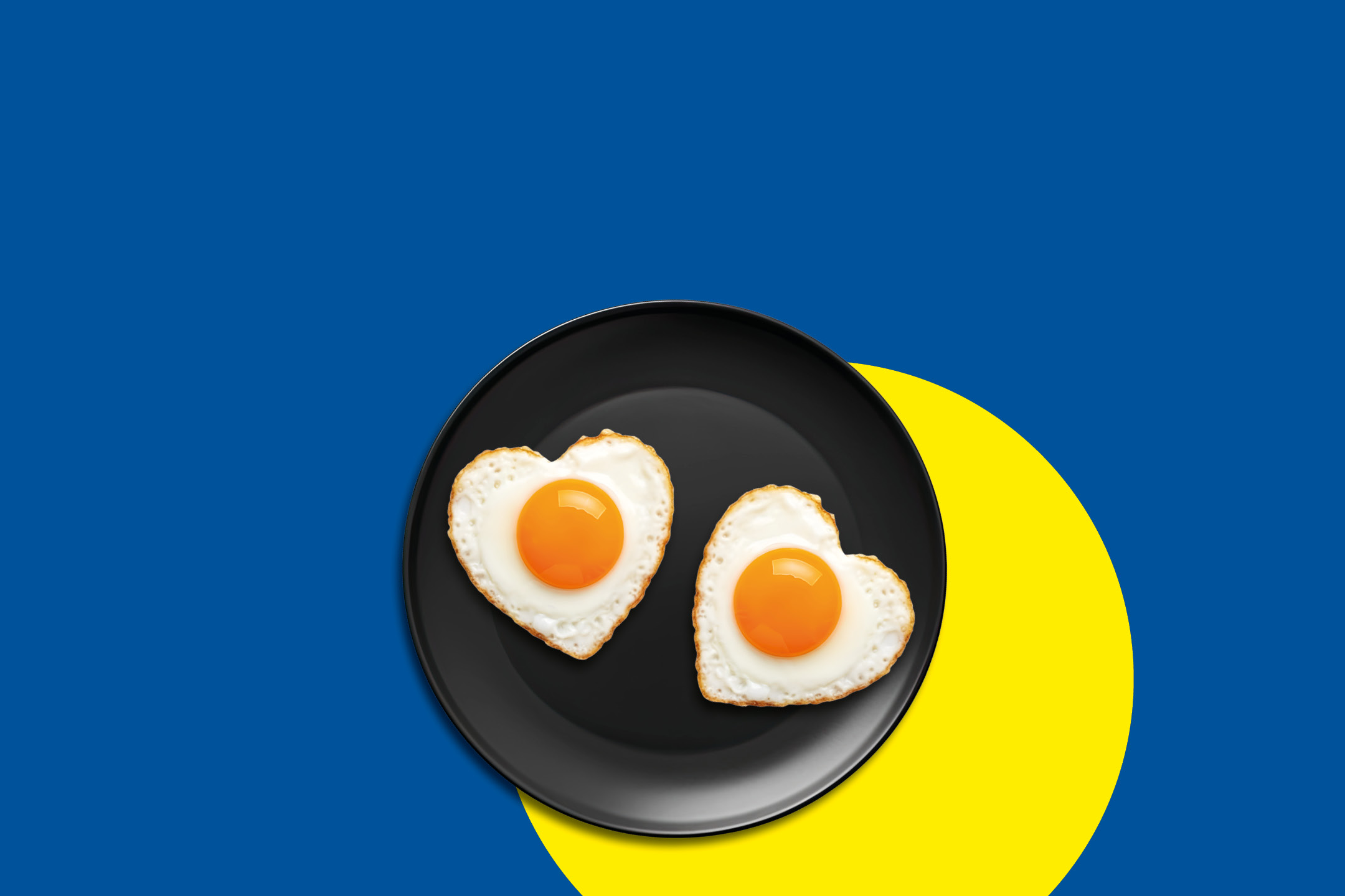 Two heart-shaped fried eggs on a black plate, set against a blue and yellow background.