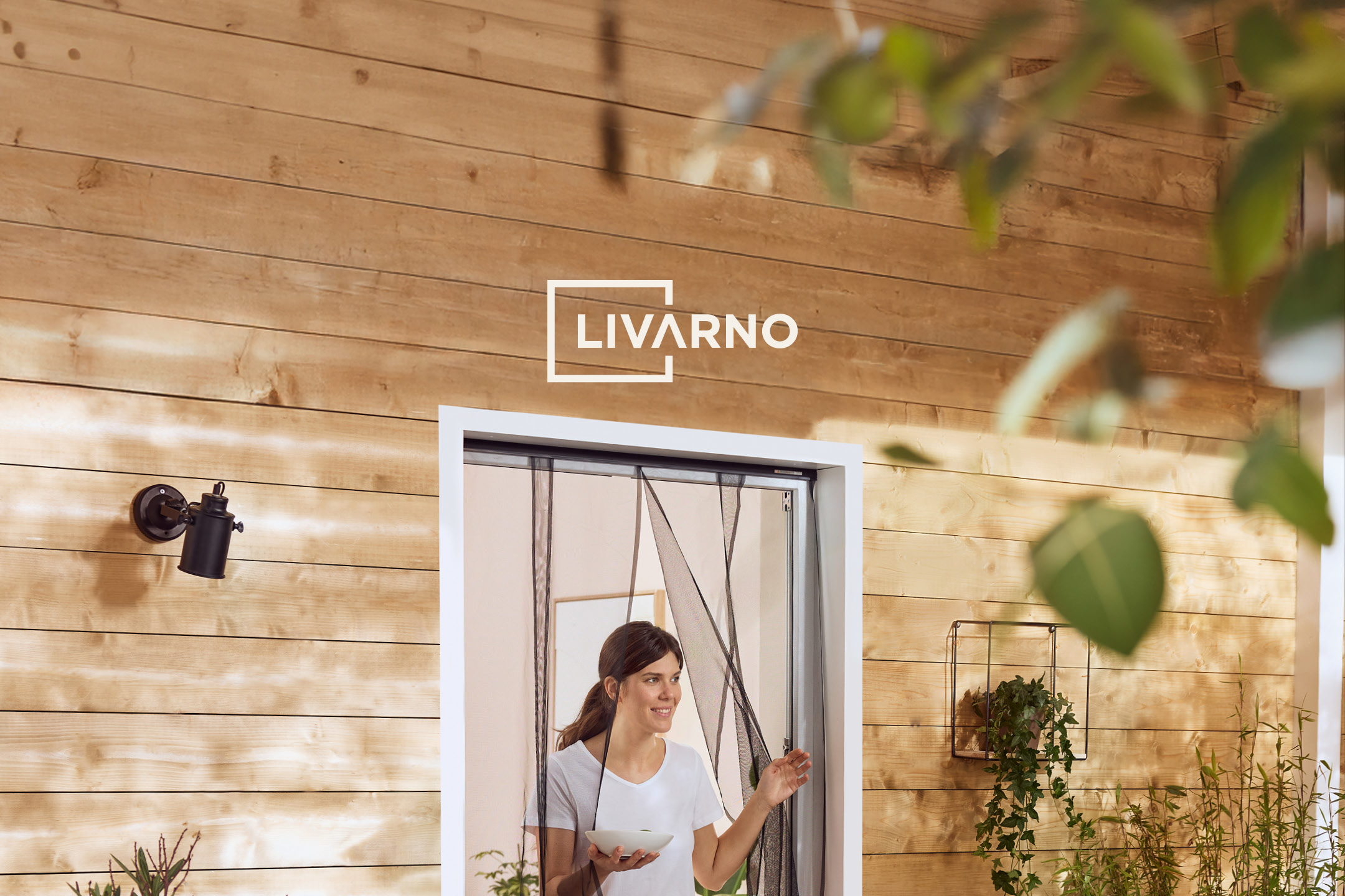 Woman opening a magnetic insect screen door on a wooden wall, with plants nearby.