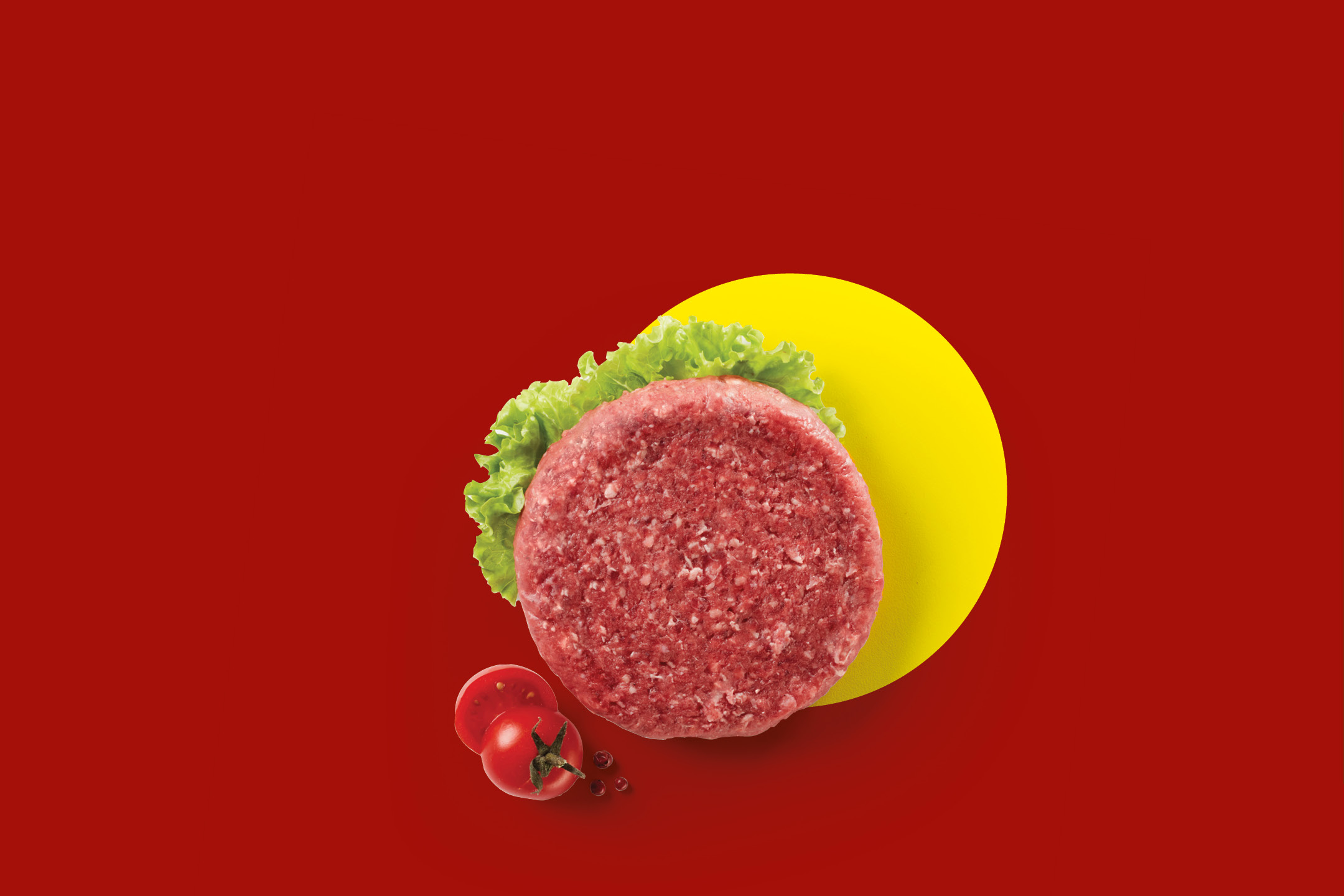 Raw beef burger patty with lettuce, tomatoes, and peppercorns on a red background.