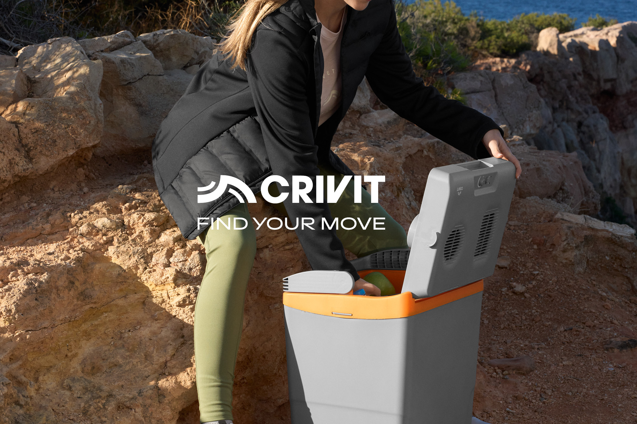 Woman opening a portable cooler outdoors, surrounded by rocks and nature.