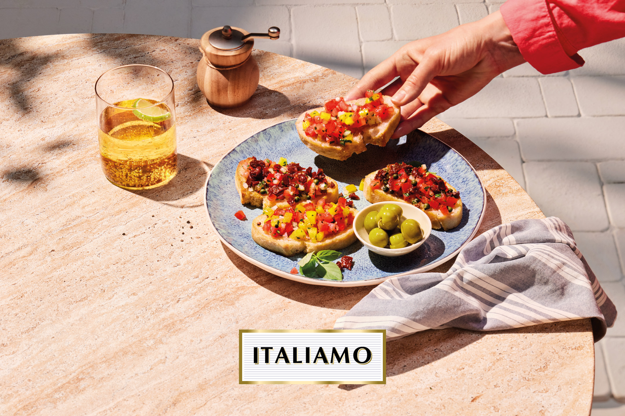 Bruschetta with various toppings, olives, and a drink on a stone table, with text 'ITALIAMO'.