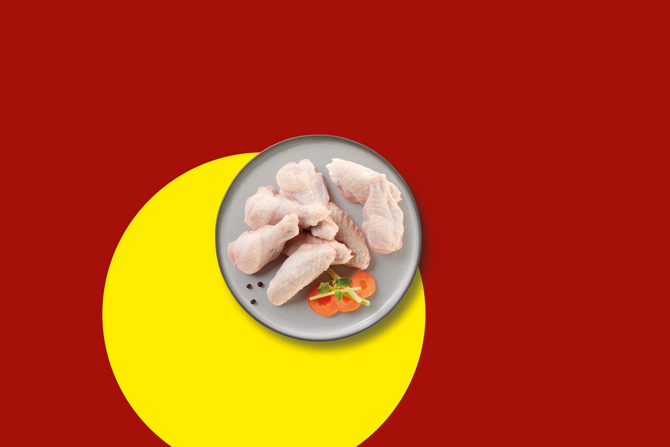 Raw chicken wings and drumettes on a grey plate with carrot slices and herbs.
