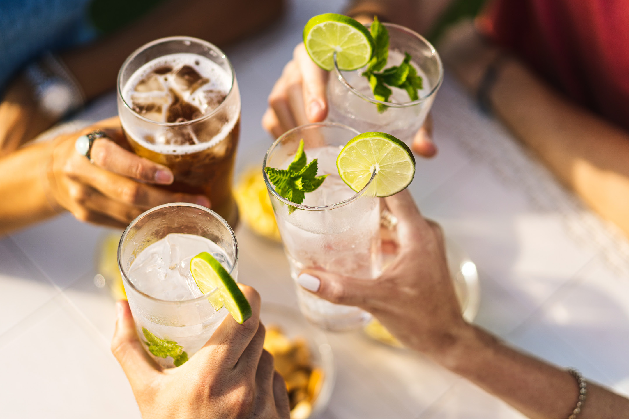 Four people toasting with refreshing drinks, including beer and cocktails with lime and mint.