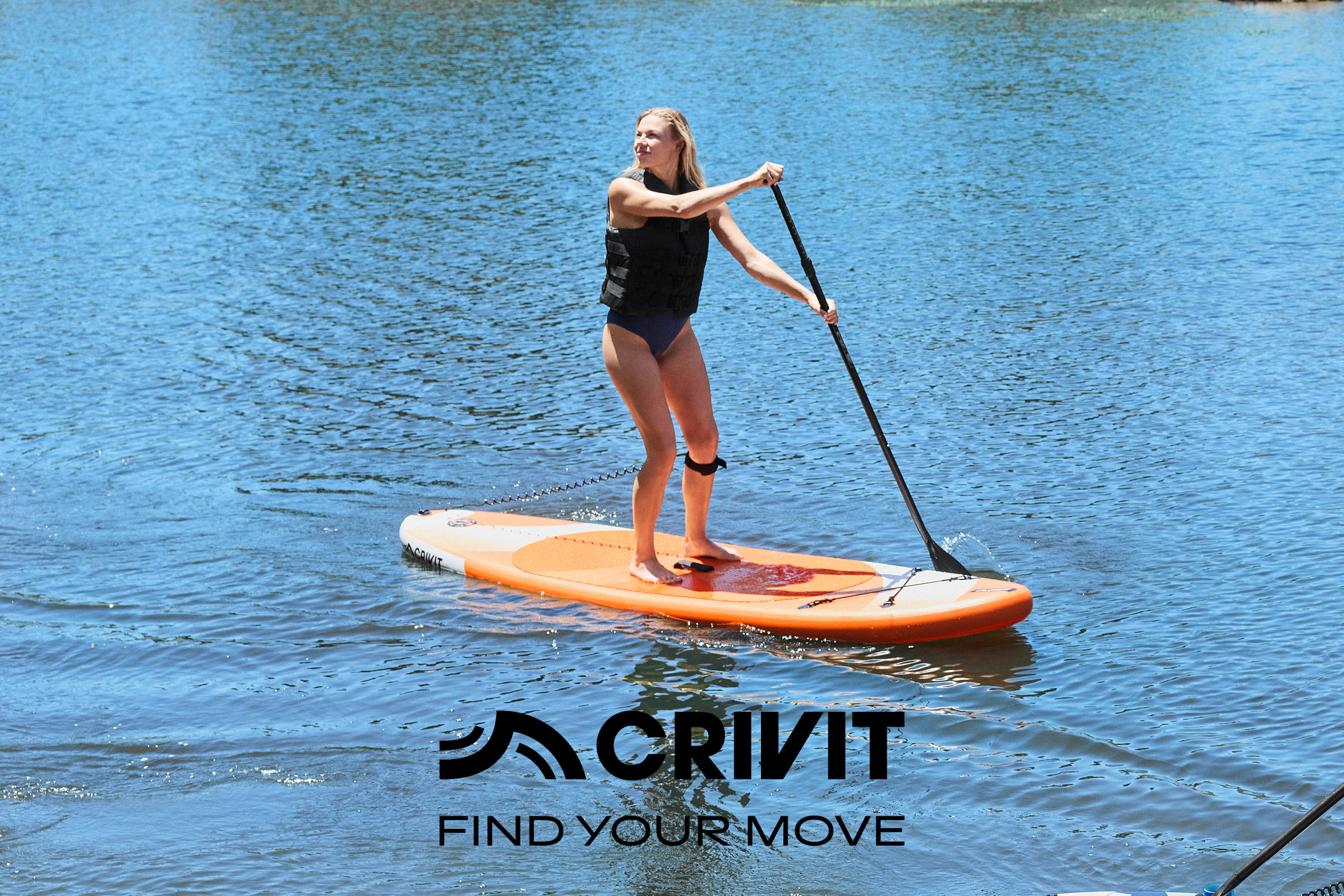 Woman paddleboarding on a lake, wearing a life vest and swimsuit.