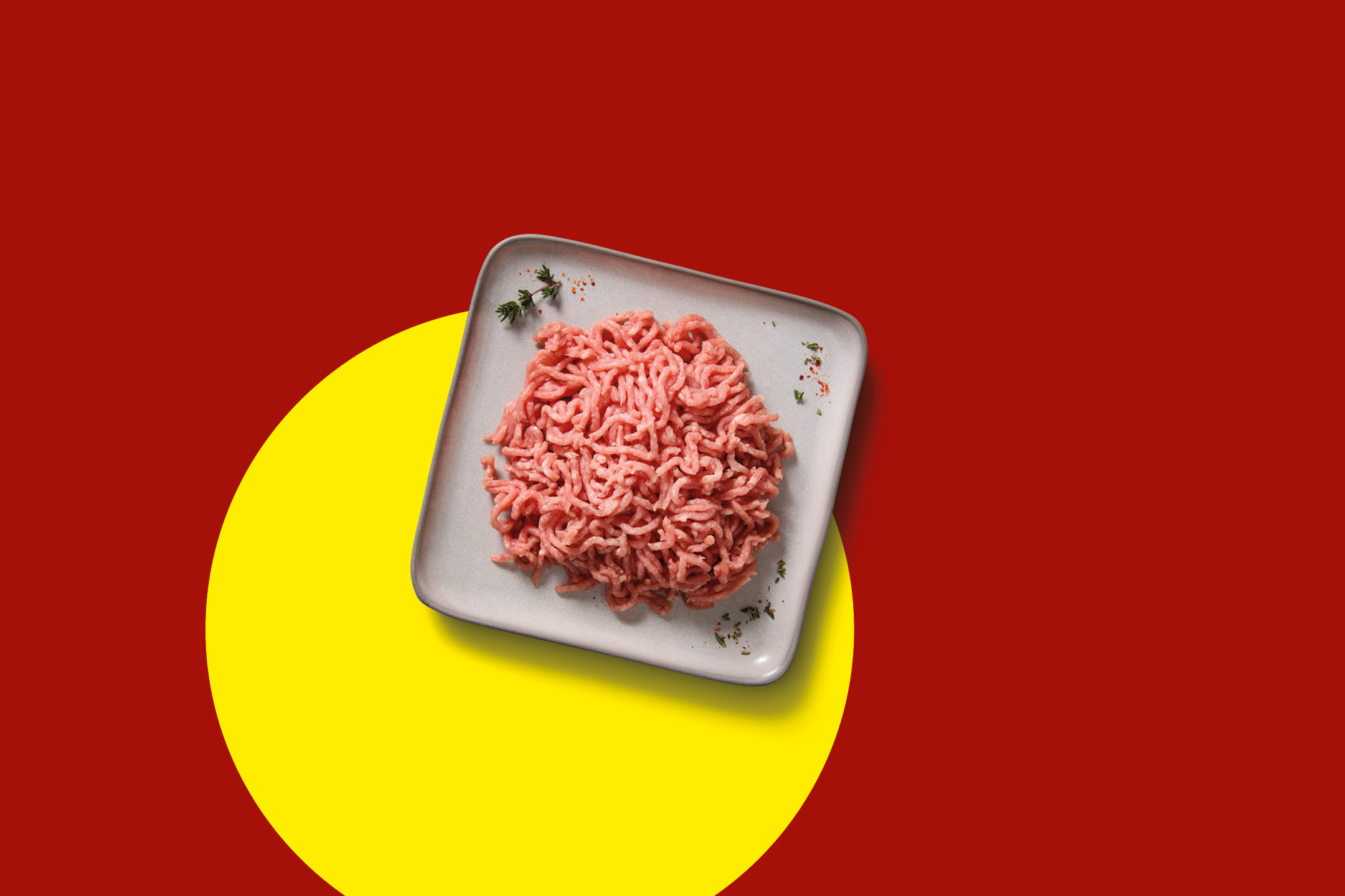 Raw minced meat on a grey plate with herbs, on a red and yellow background.