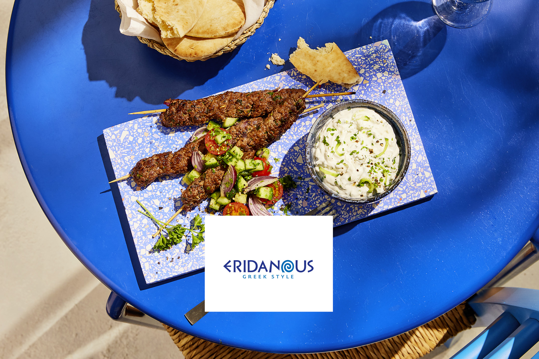 Kofta kebabs with tzatziki, salad, and pita bread on a blue table