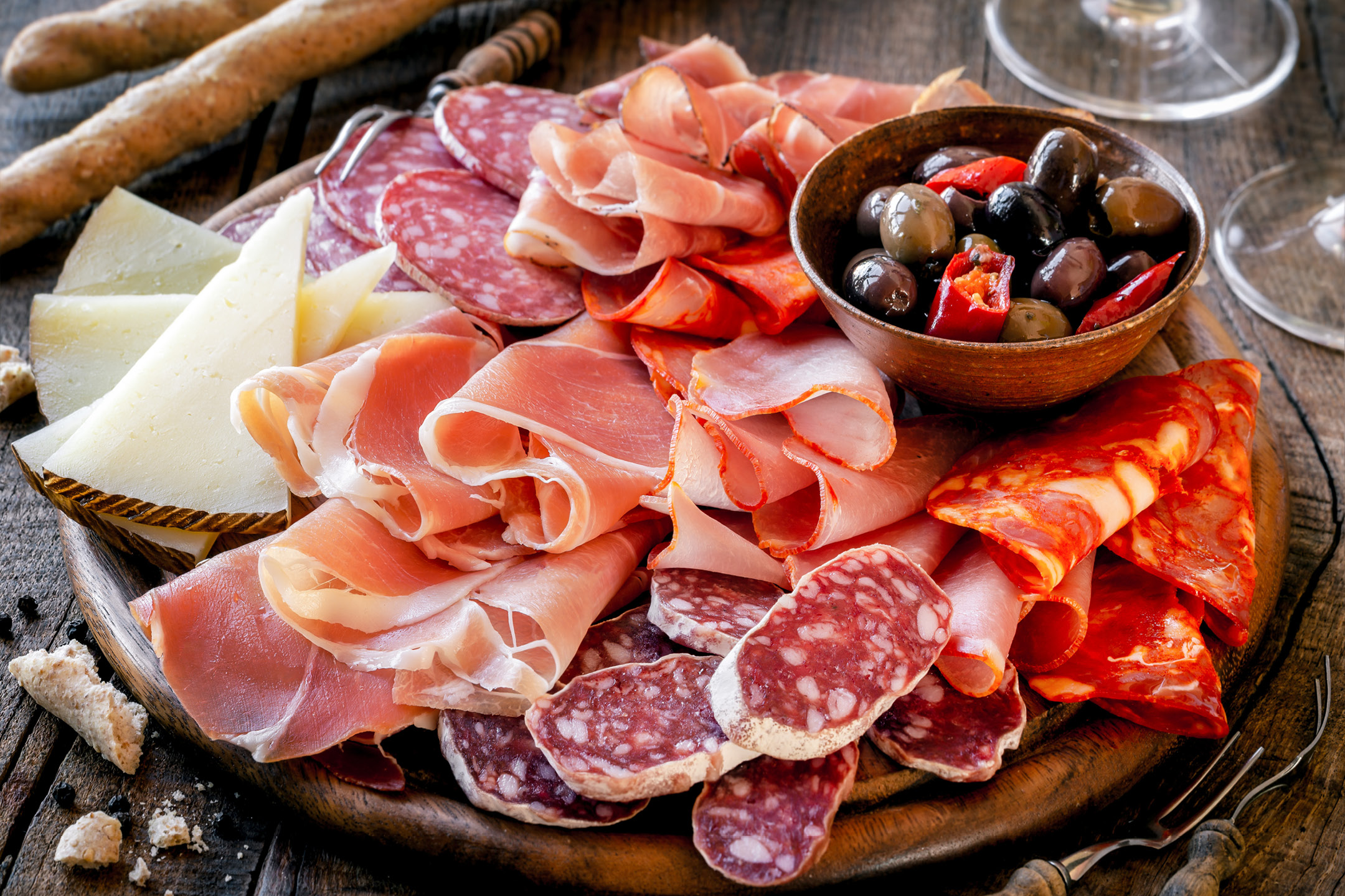 Charcuterie board with various cured meats, cheeses, olives, and breadsticks.