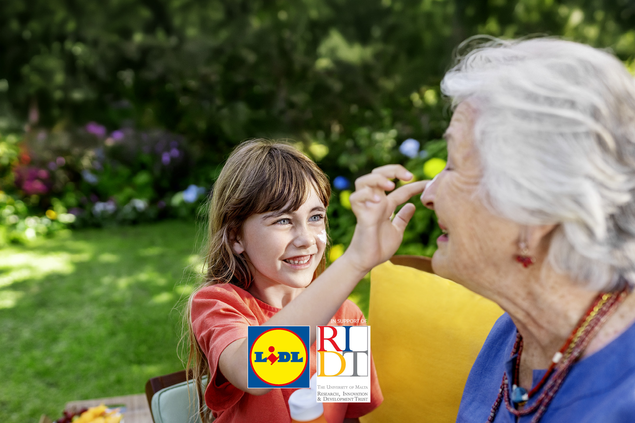 A young girl applies sunscreen to an older woman's face in a sunny garden.