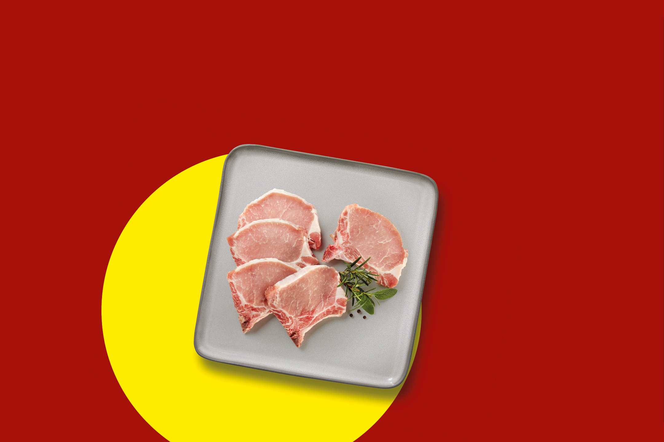 Raw pork chops with herbs and spices on a grey plate, against a red and yellow background.