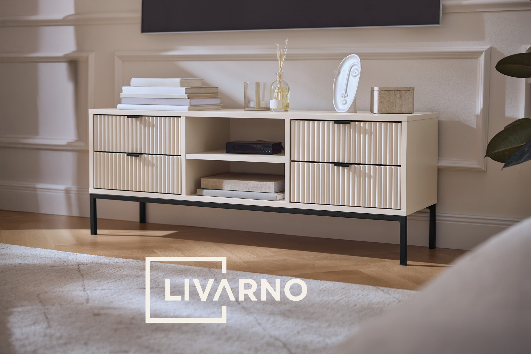 Cream-colored TV stand with fluted drawers, styled with books, a diffuser, and decor.