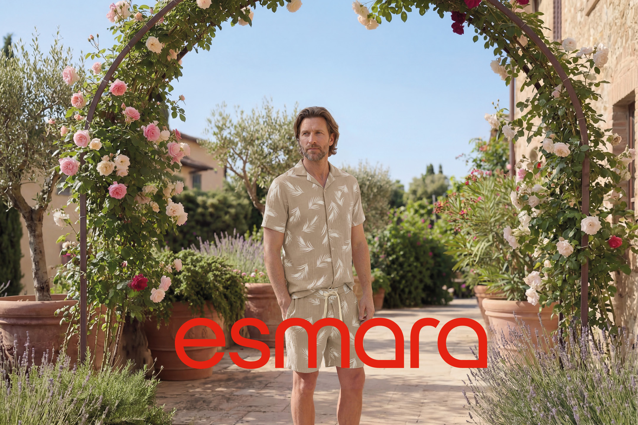 Man in a beige leaf-patterned shirt and shorts, standing under a rose archway.
